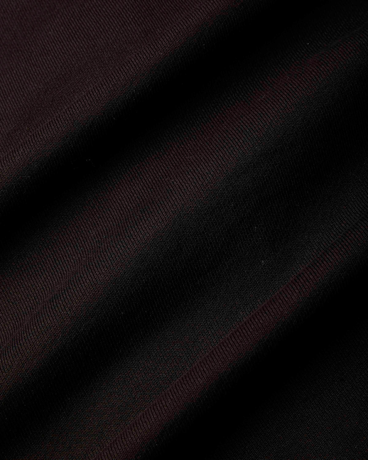 A close-up of dark fabric with a subtle diagonal twill texture, showing deep black and very dark burgundy folds.