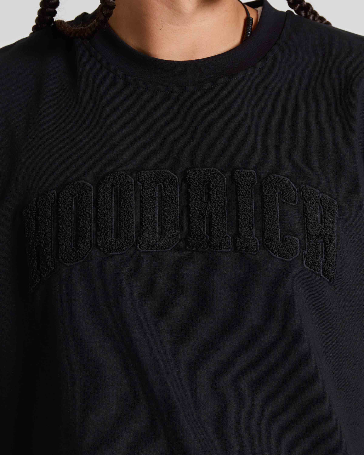 Close-up of a person wearing a black crewneck sweatshirt with 'HOODRICH' embroidered in black across the chest.