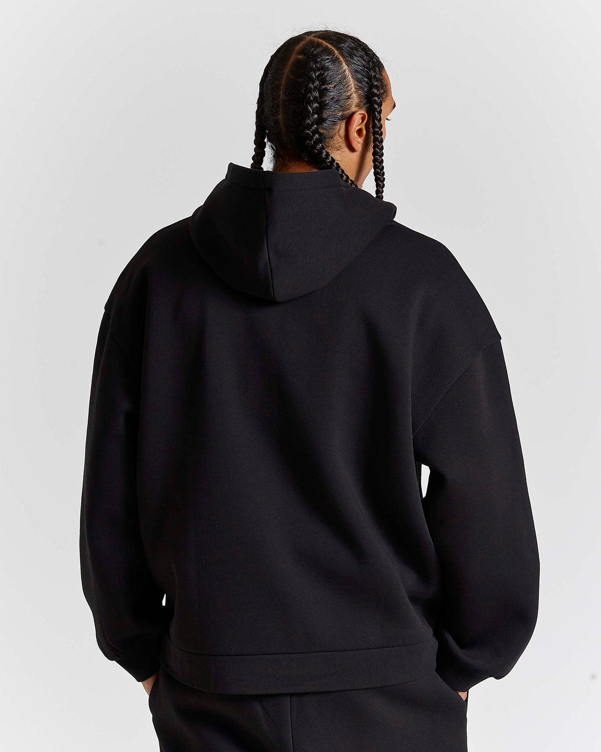 A person shown from the back wearing a black pullover hoodie and matching black pants against a light gray studio background.