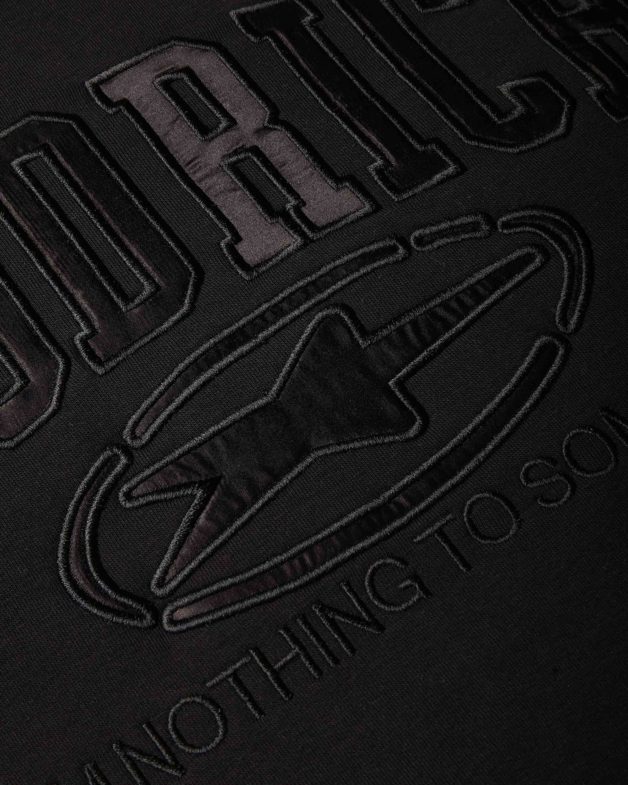 Close-up of a black fabric surface with large tonal embroidered lettering and a star-like emblem, showing partial text on HOODRICH.
