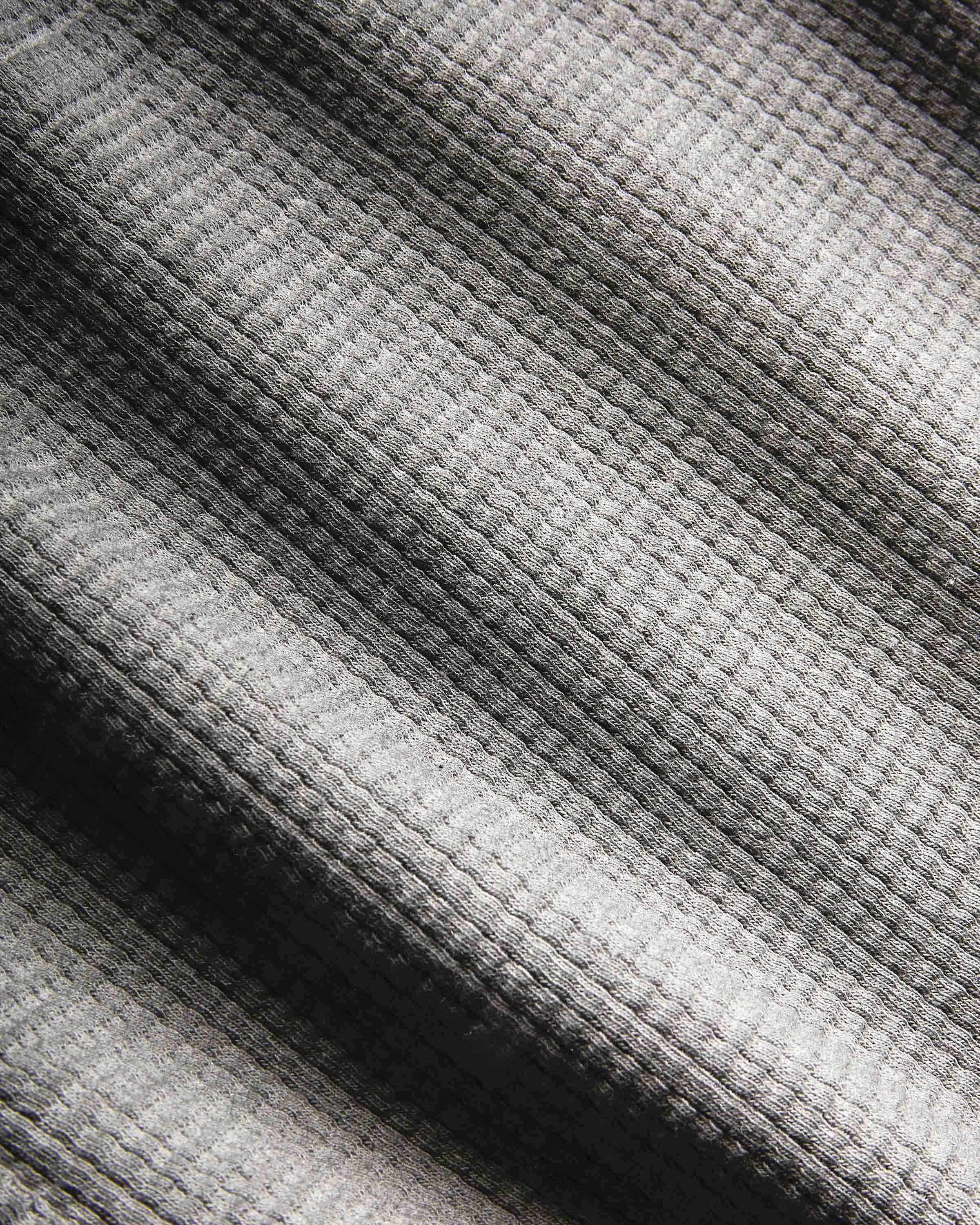 Close-up of a waffle-knit fabric with a striped pattern in shades of gray, black, and off-white.