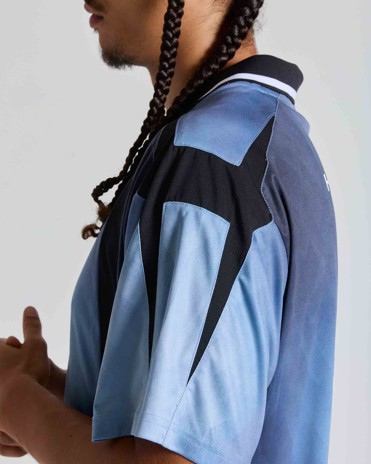 A close-up side profile of a person wearing a short-sleeve athletic jersey with a colorblock design in light blue, dark blue, and black, featuring a star motif on the back.