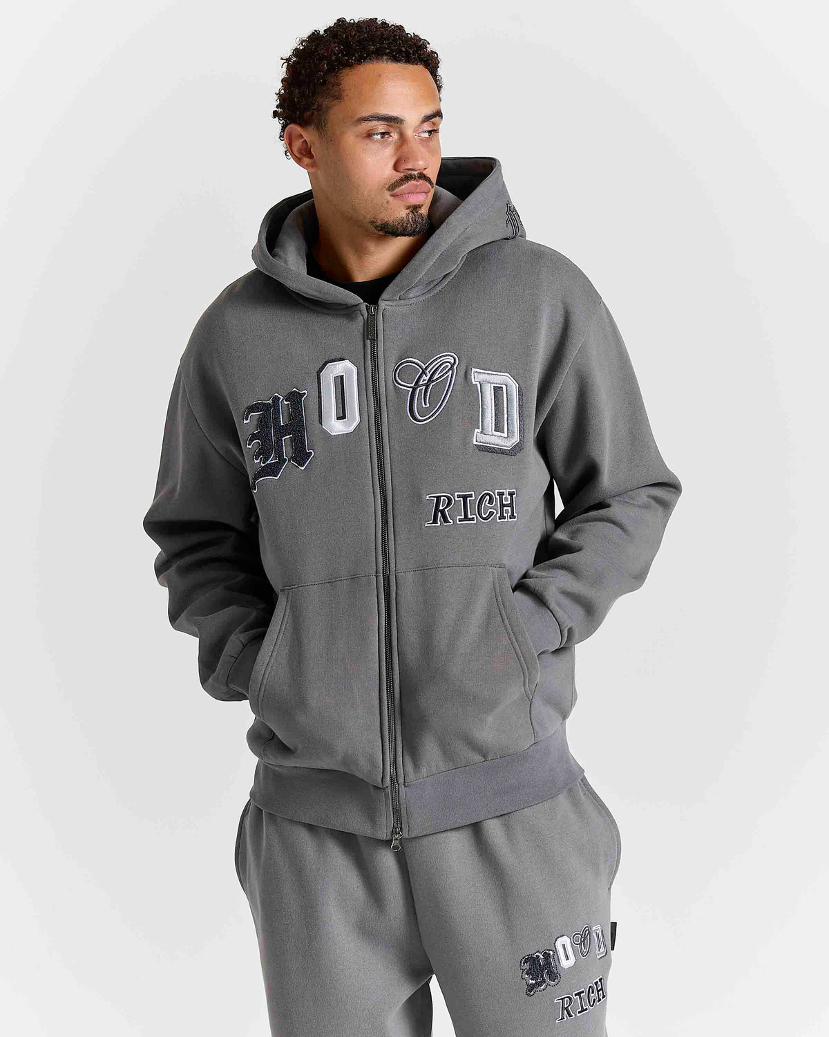Displays a model wearing the grey lava smoke 'Hoodrich' branded Forza Oversized Zip Through Hoodie