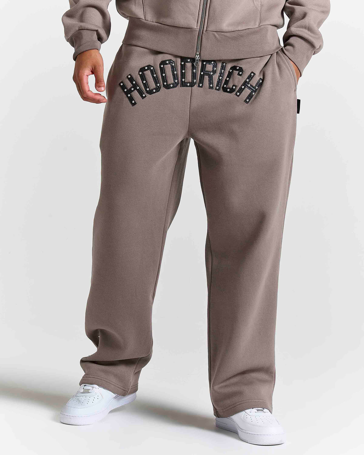Displays a model wearing the Brown 'Hoodrich' branded men's Varso Studs Full Tracksuit
