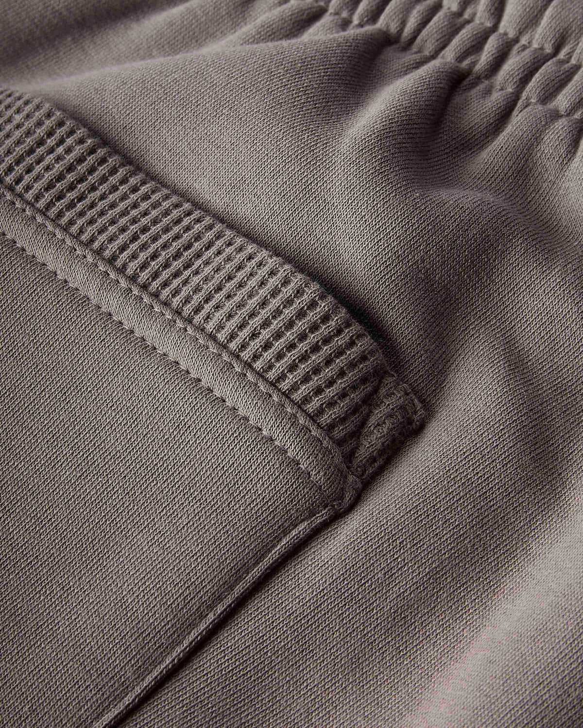 Close-up detail of a pair of gray sweatpants showing the elastic waistband and a ribbed pocket opening.