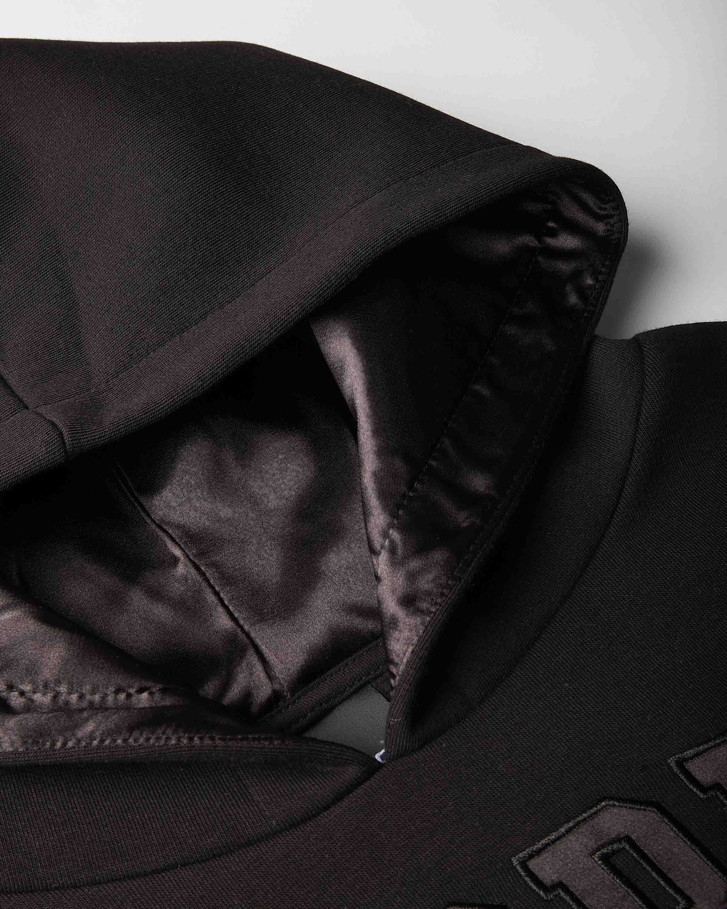 Close-up of a black hooded sweatshirt showing the interior lining of the hood and shoulder area against a light gray background.