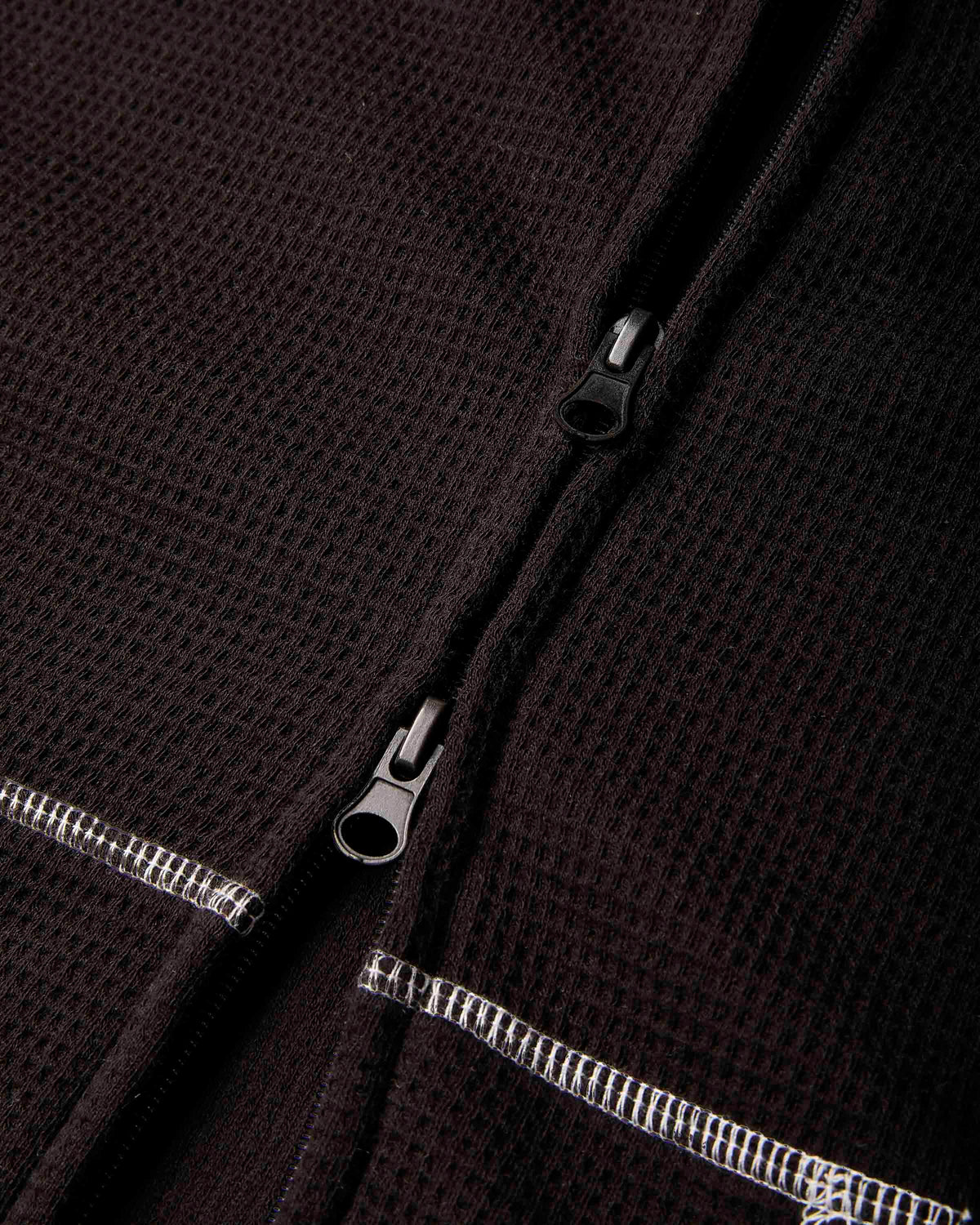 Close-up of a dark brown waffle-knit zippered garment, showing the textured fabric and silver-toned zipper pulls.
