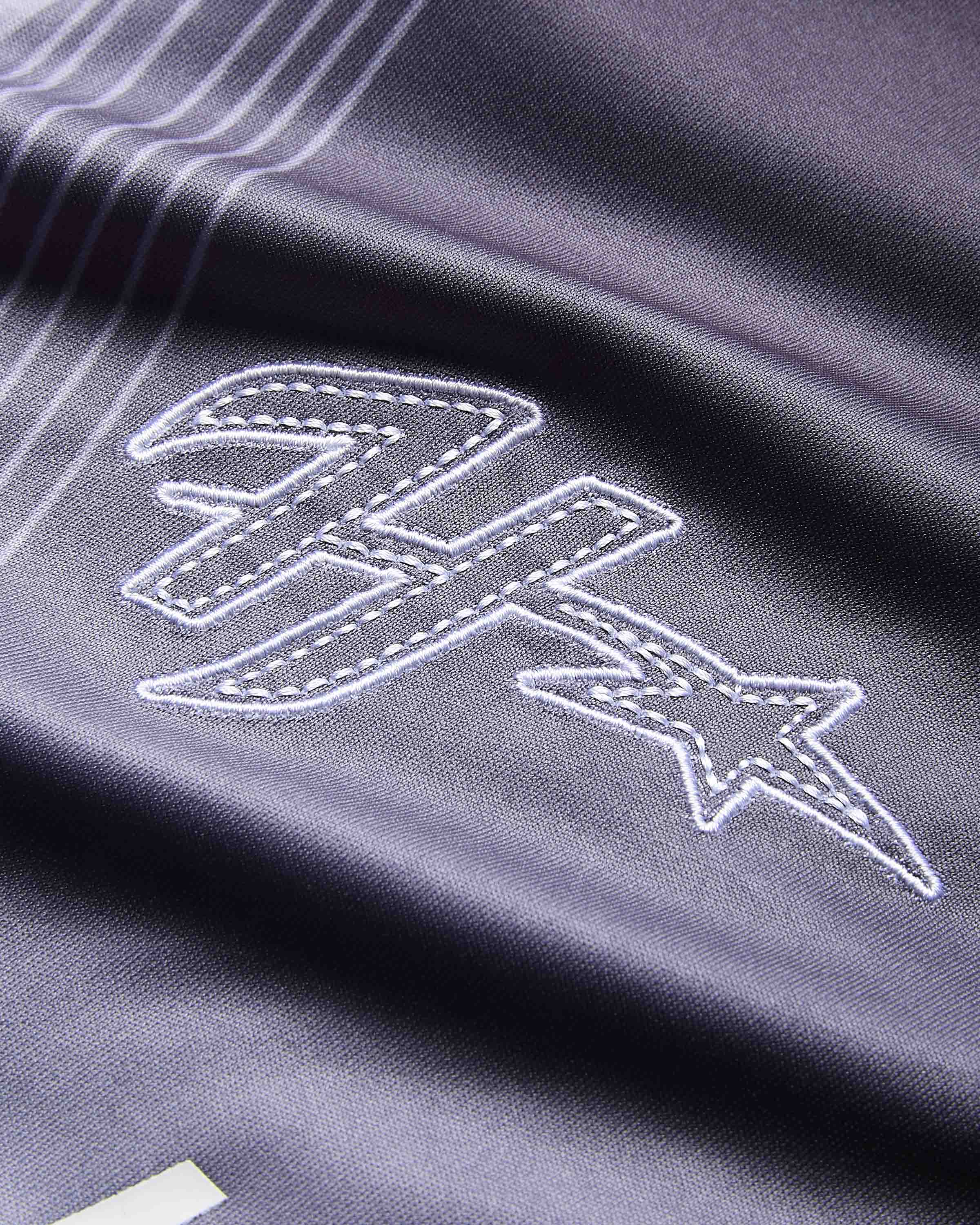 Close-up of a dark gray or black athletic fabric with white embroidered logo details, showing a stylized letter 'H' and star motif.