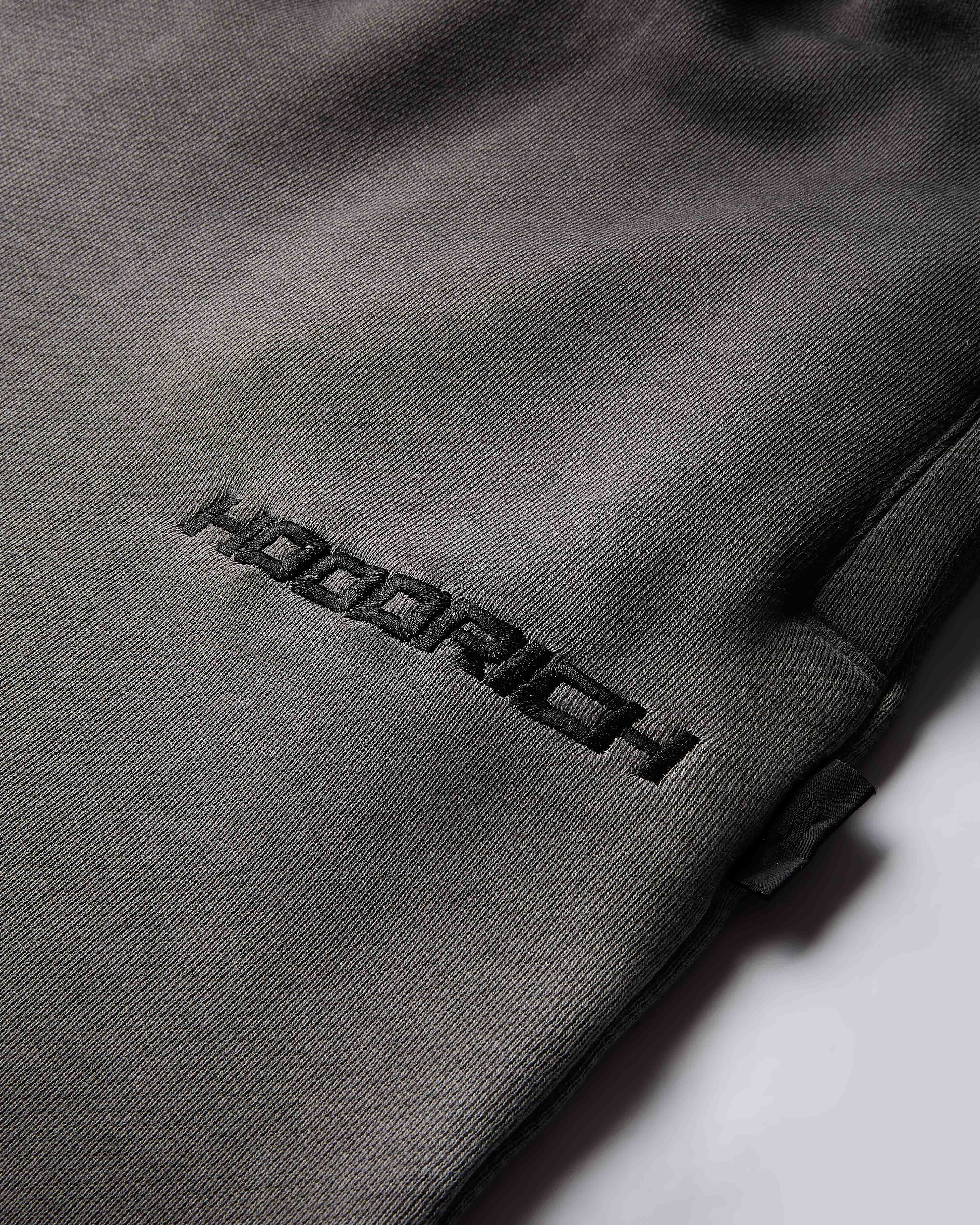 Close-up of the black Hoodrich logo embroidered on the black oil wash fabric of the shorts.