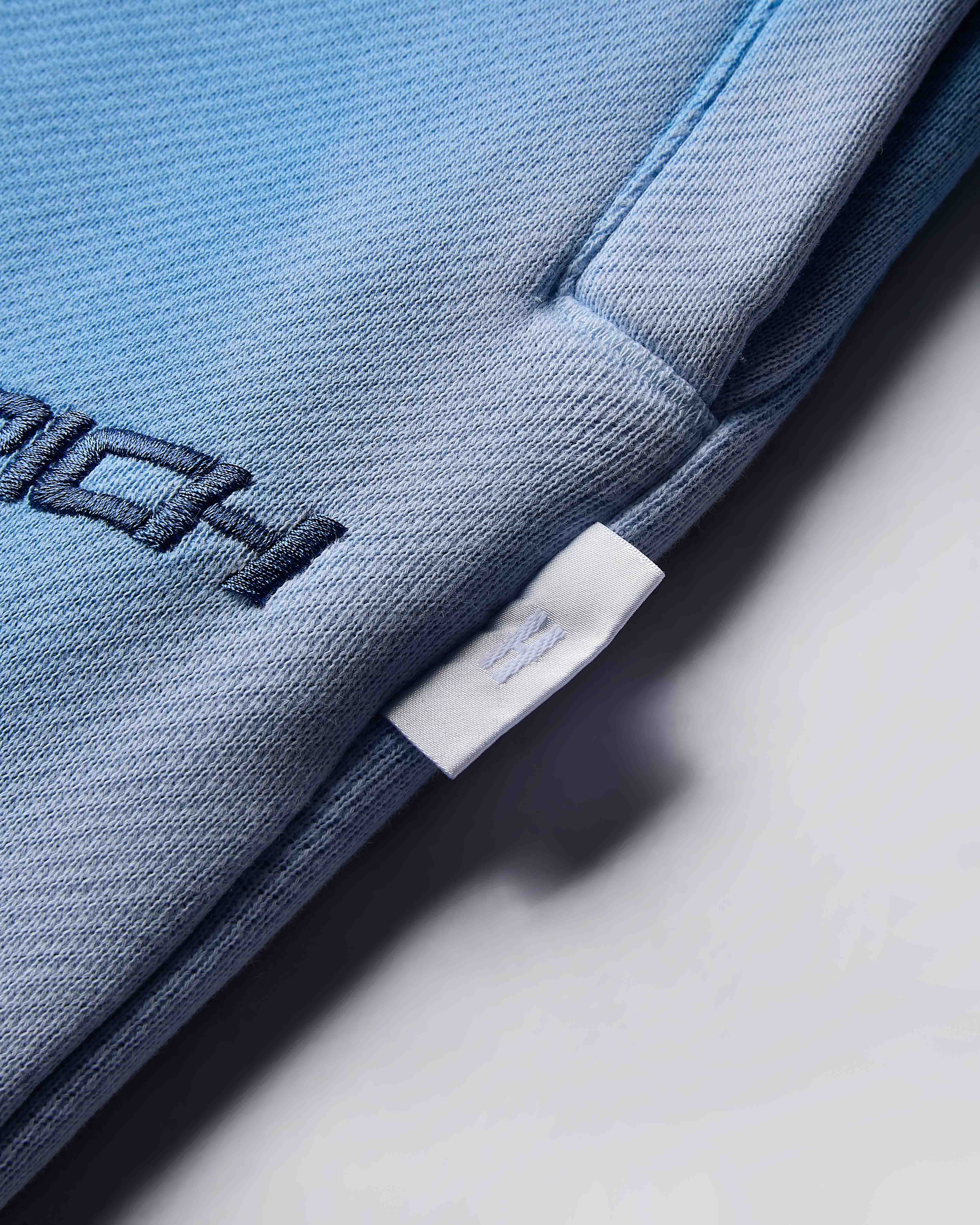 Close-up of a blue garment with a brand label on a light gray background