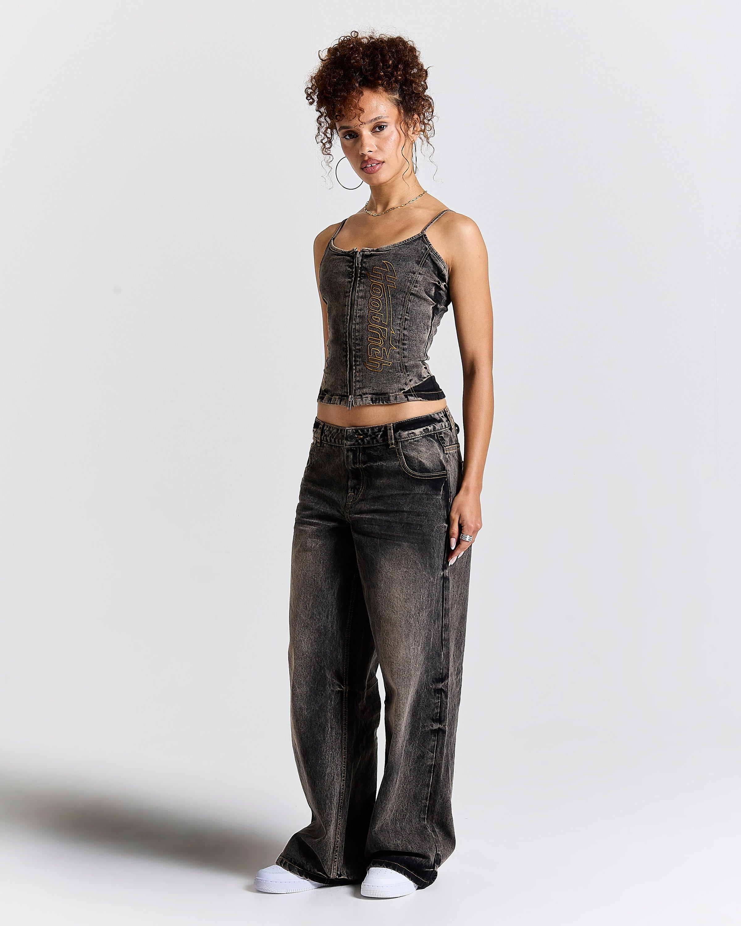 Model wearing a fitted black denim corset top and matching baggy jeans with yellow Hoodrich logo embroidery.