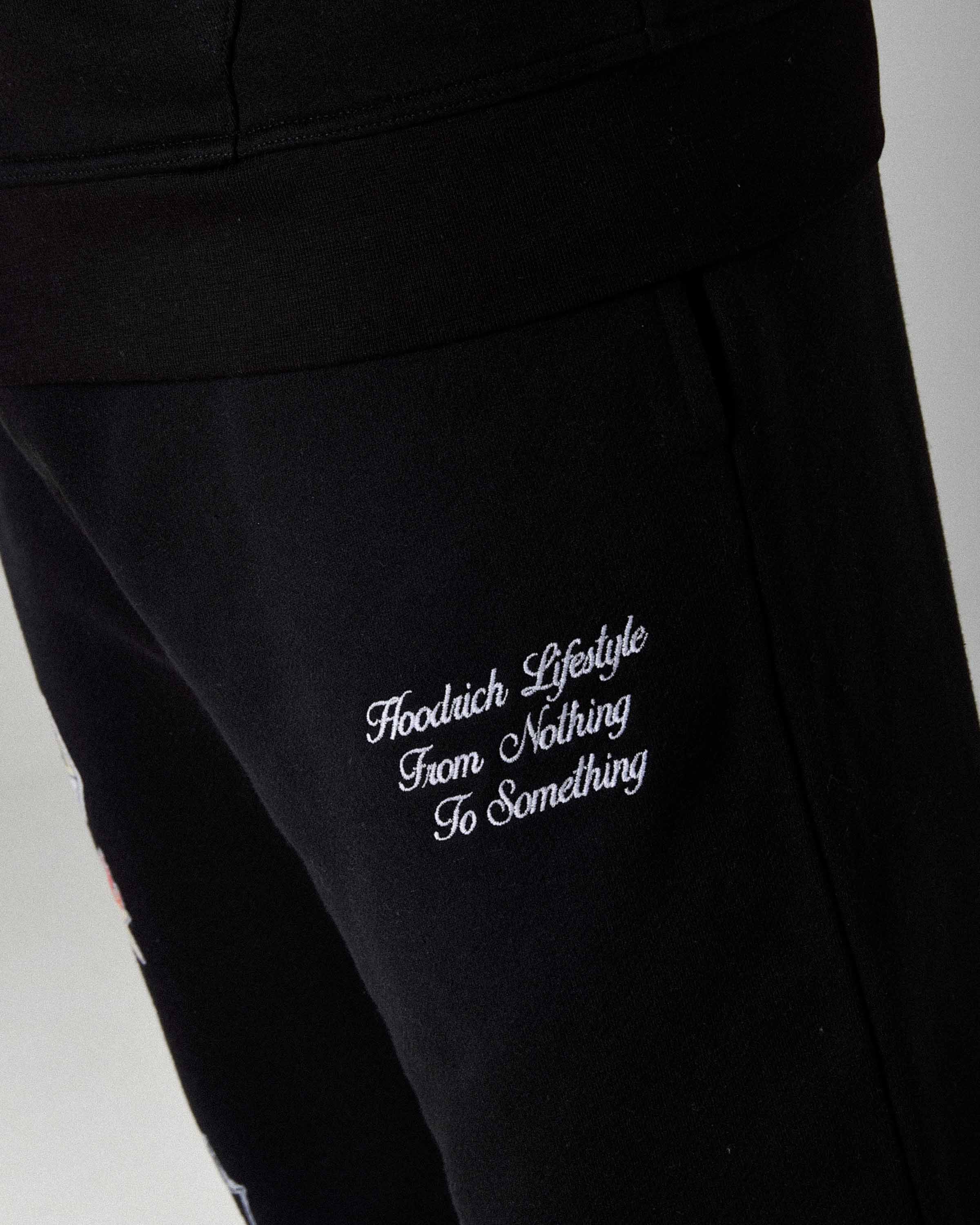 Displays a model wearing the Black 'Hoodrich' branded men's The Winner's Circle Phase Full Tracksuit
