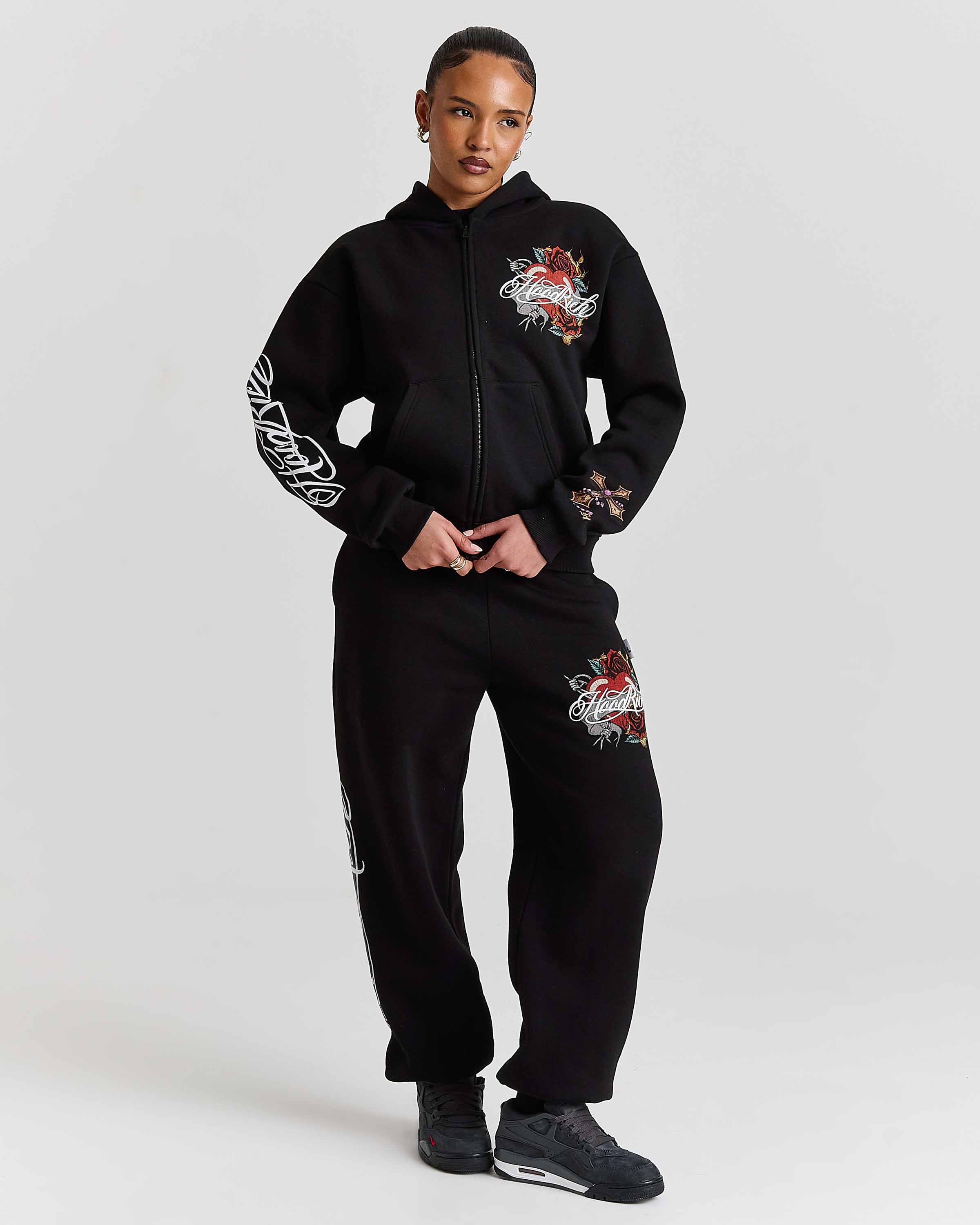Person wearing a black hoodie and pants with floral designs on a white background