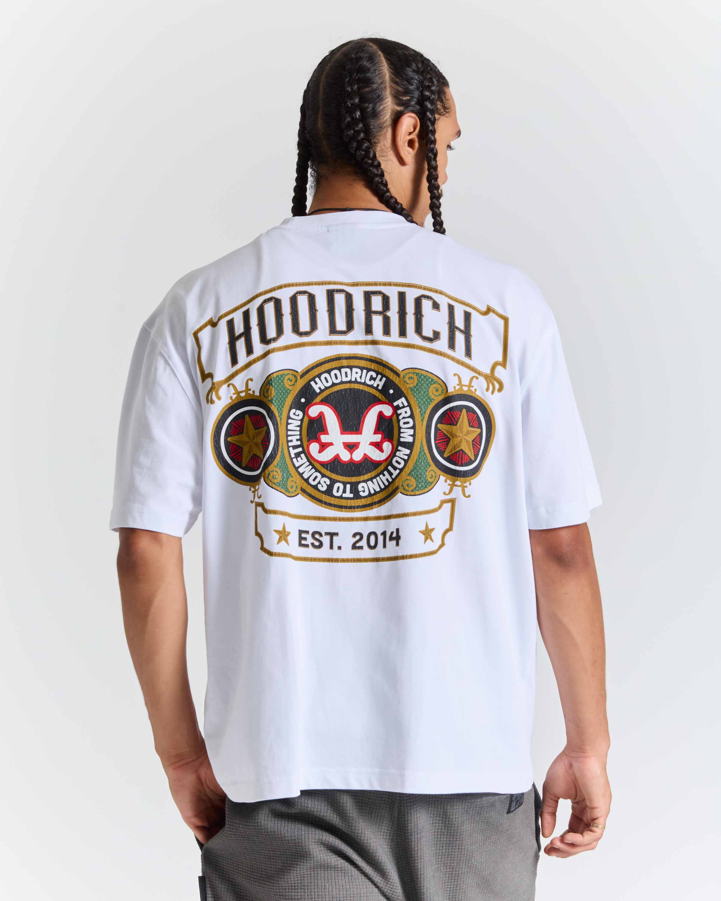 A man shown from the back wearing a white HOODRICH t-shirt with a large graphic print on the back, paired with gray sweatpants against a light gray studio background.