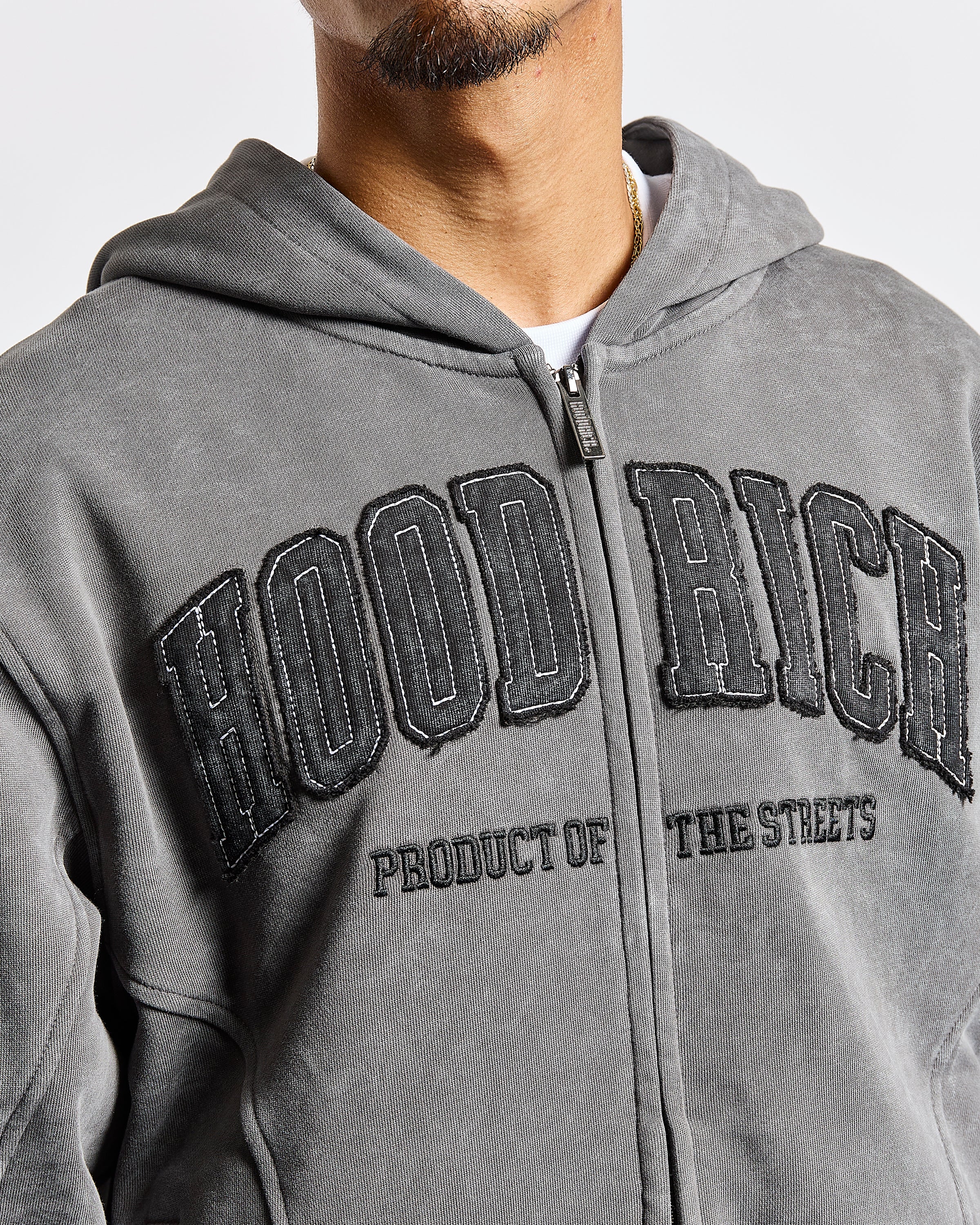 A close-up of a person wearing a gray zip-up hoodie with distressed black 'HOOD RICH' lettering across the chest.
