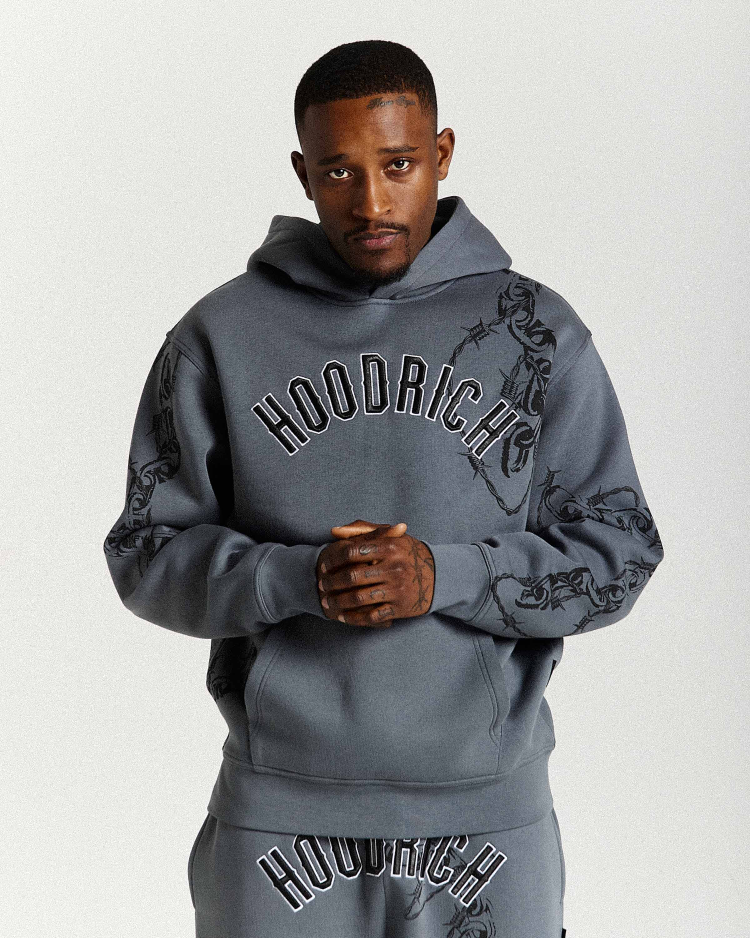 Man wearing a gray 'Hoodrich' hoodie and pants on a white background