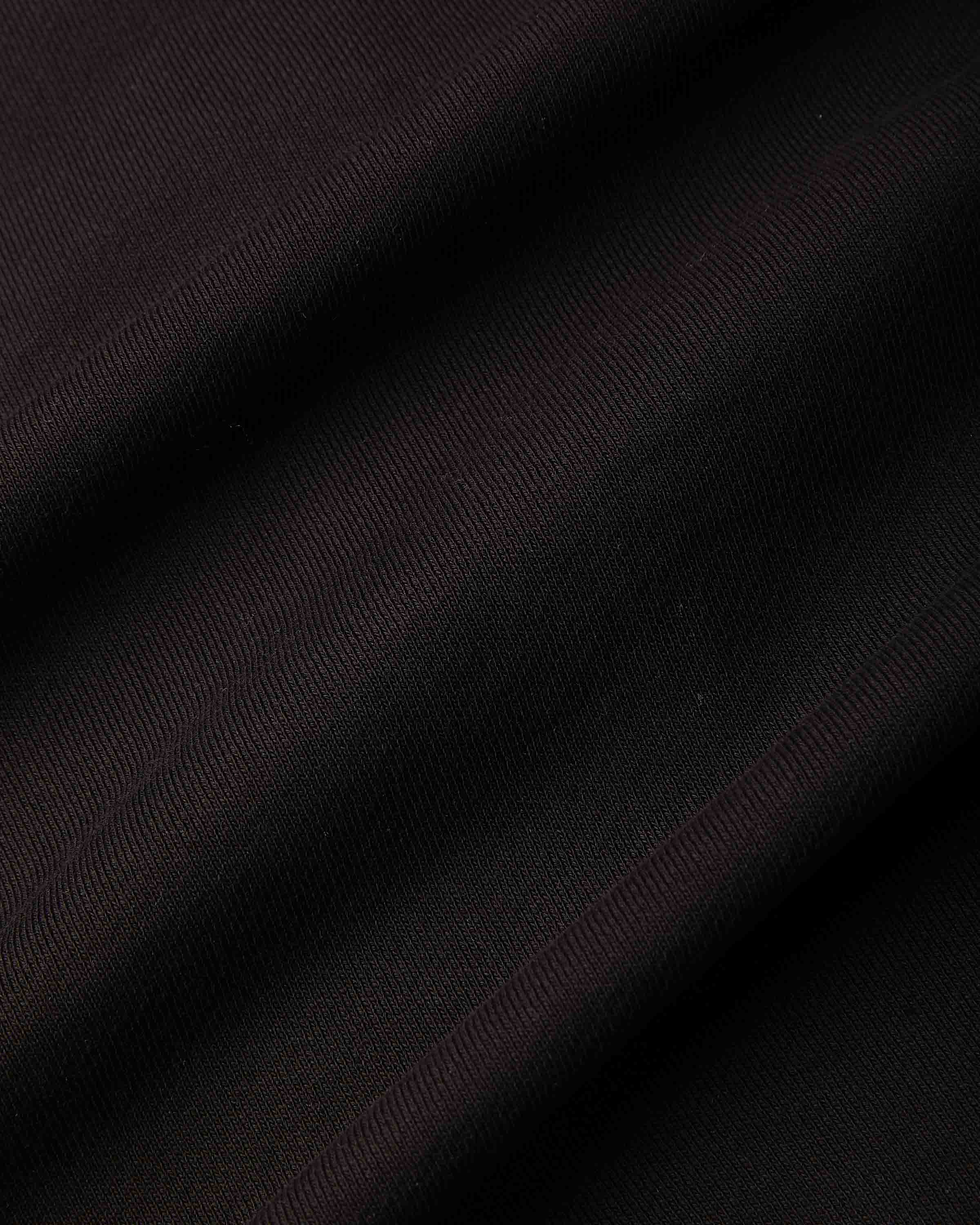 A close-up of dark fabric with a subtle diagonal twill texture, showing deep black and very dark burgundy folds.