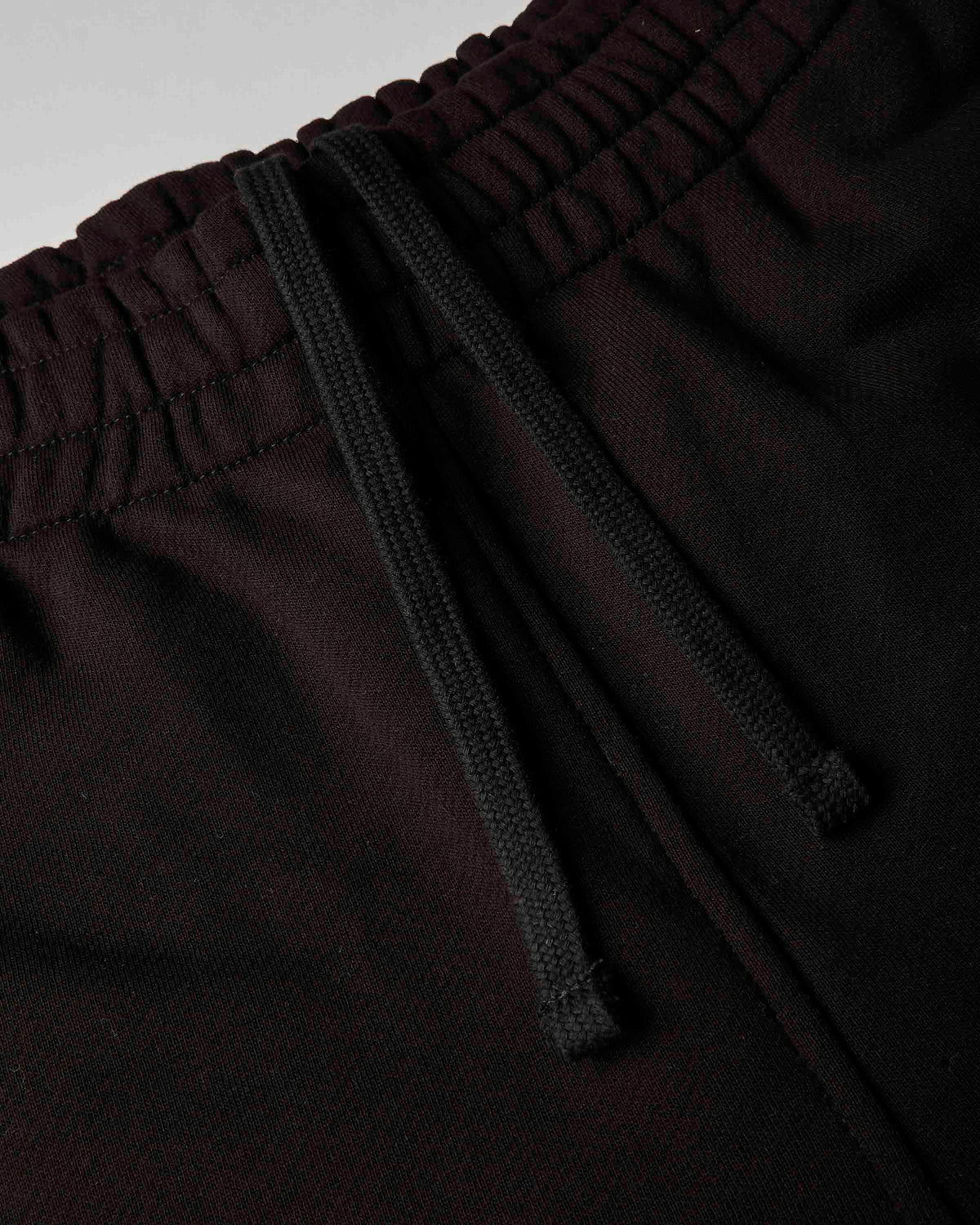 Close-up of dark burgundy or very deep wine pants with a black drawstring waistband, showing the fabric texture and elasticized waist.