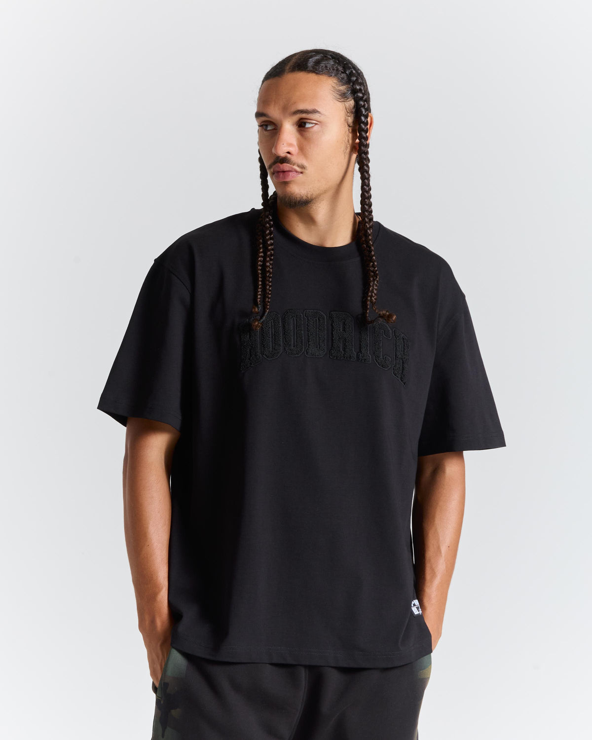 A man wearing a black short-sleeve t-shirt with tonal black 'HOODRICH' text across the chest, photographed against a light gray studio background.