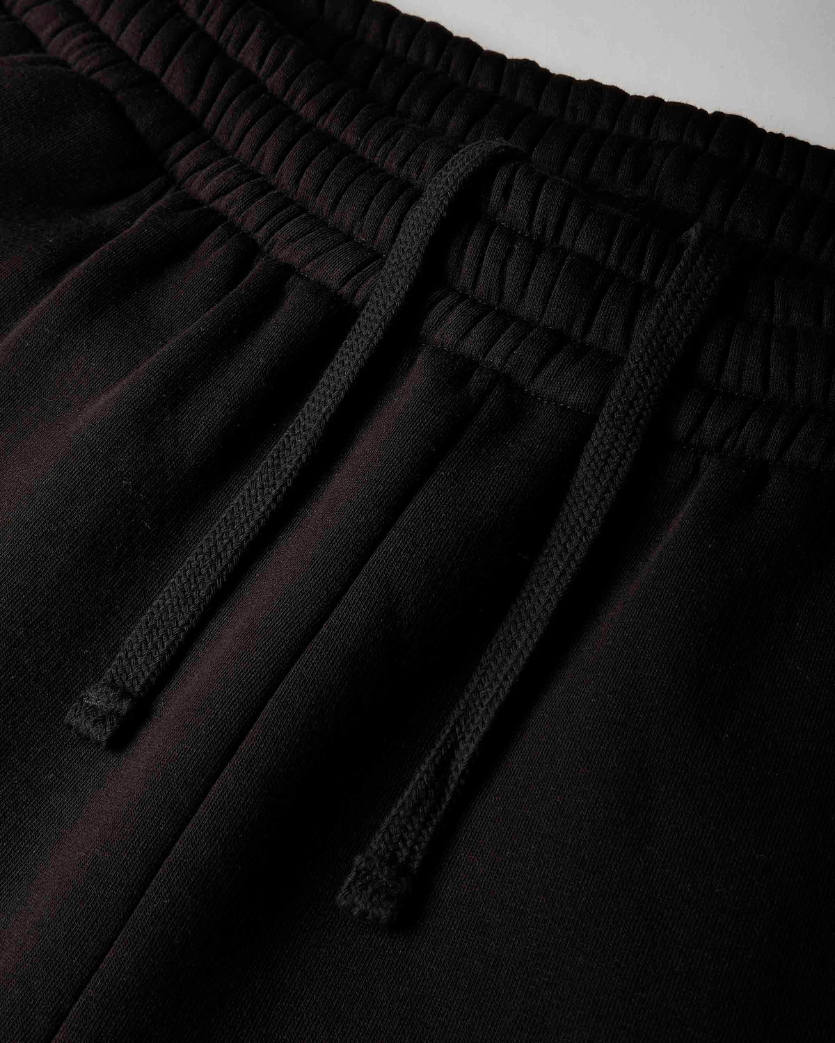 Close-up of black drawstring sweatpants showing the elastic waistband and textured drawstrings.