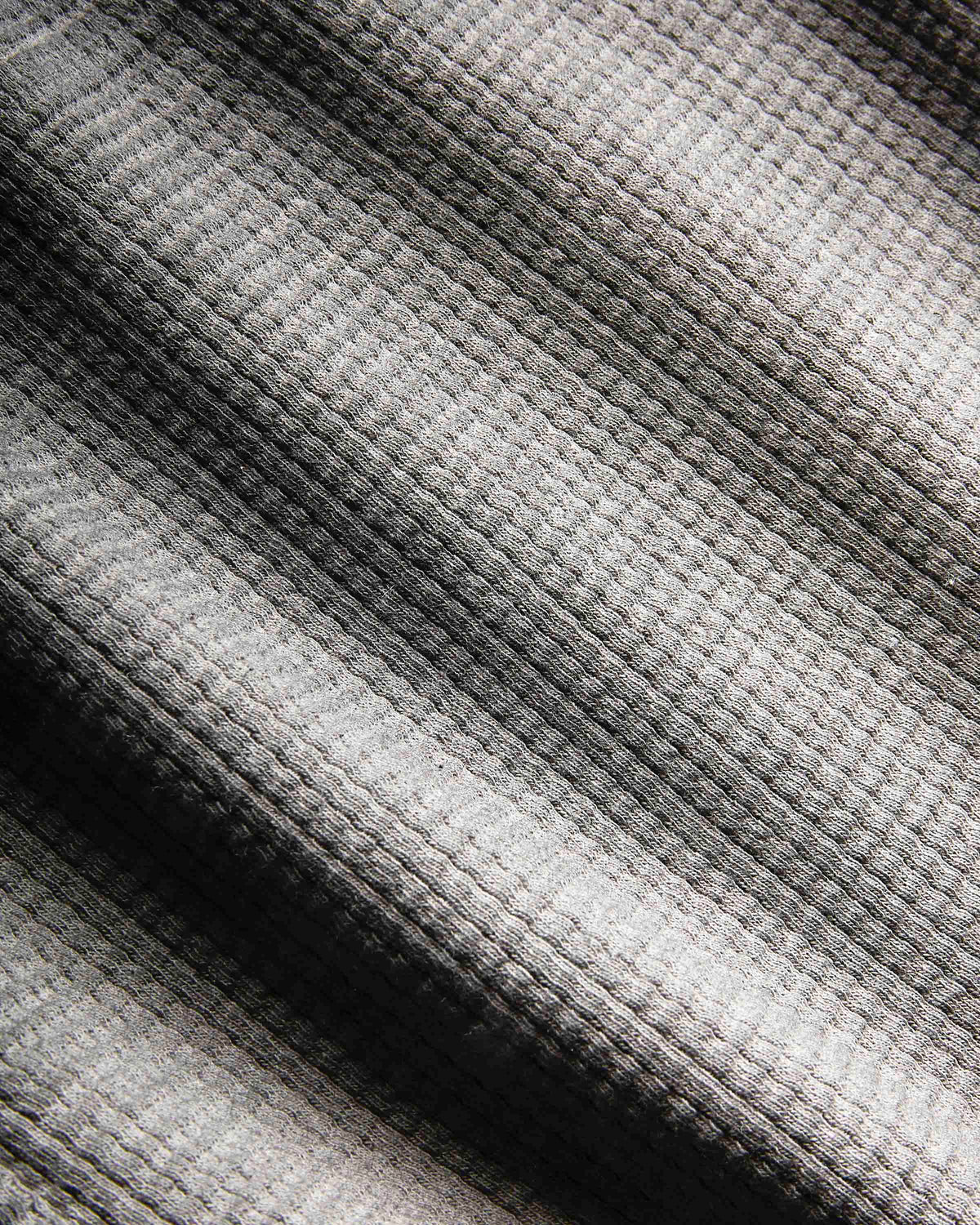 Close-up of a waffle-knit fabric with a striped pattern in shades of gray, black, and off-white.