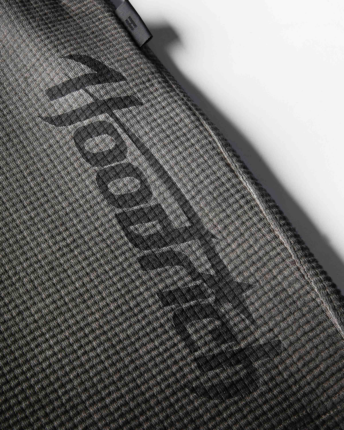 Close-up of a dark gray textured fabric surface with a large black diagonal 'hoodedog' logo and a small black brand tab near the top edge.