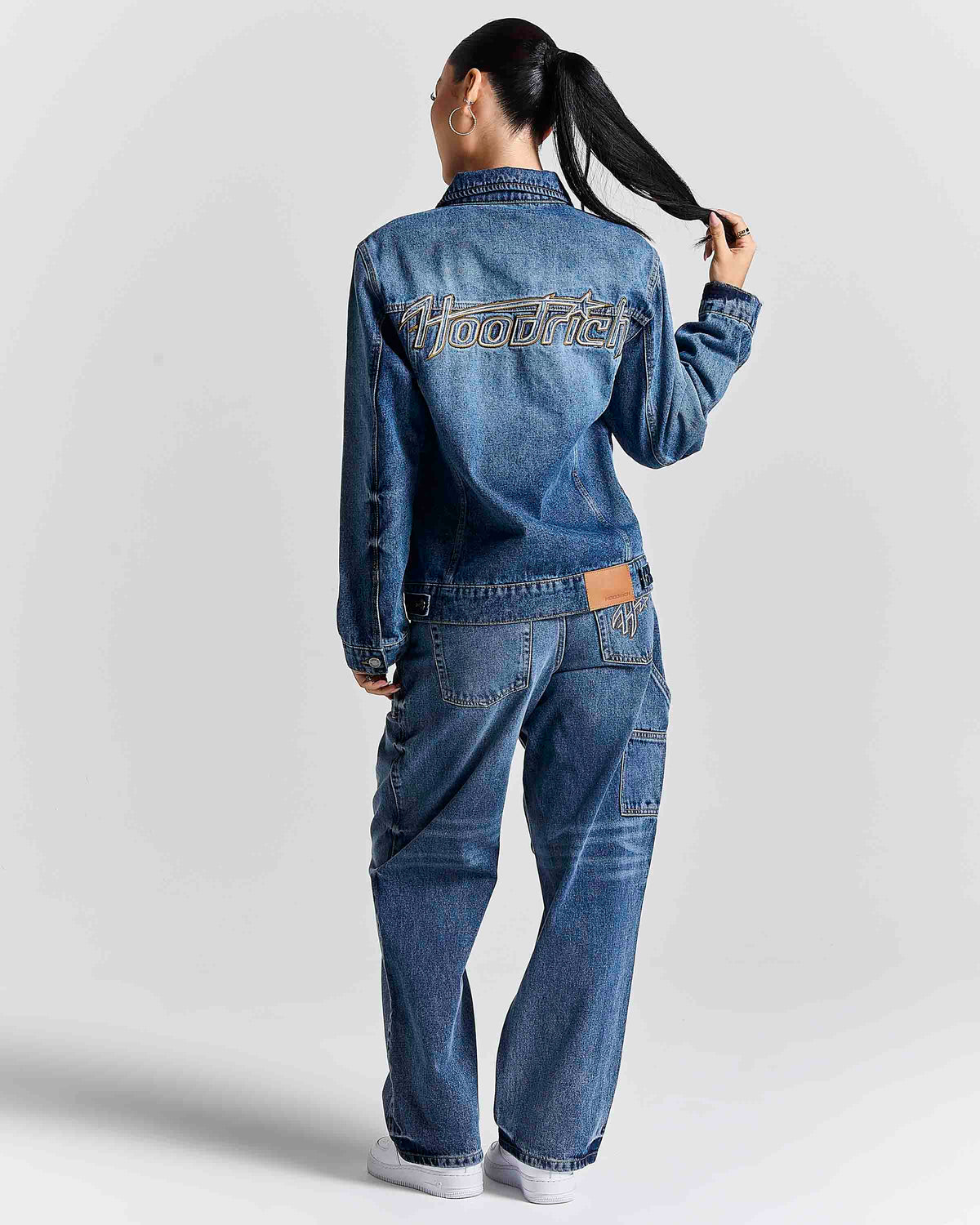 A model shown from the back wearing a blue denim jacket and matching wide-leg denim jeans. The jacket features 'hoodster' embroidered in white across the upper back, and a brown leather brand patch is visible on the back waistband.