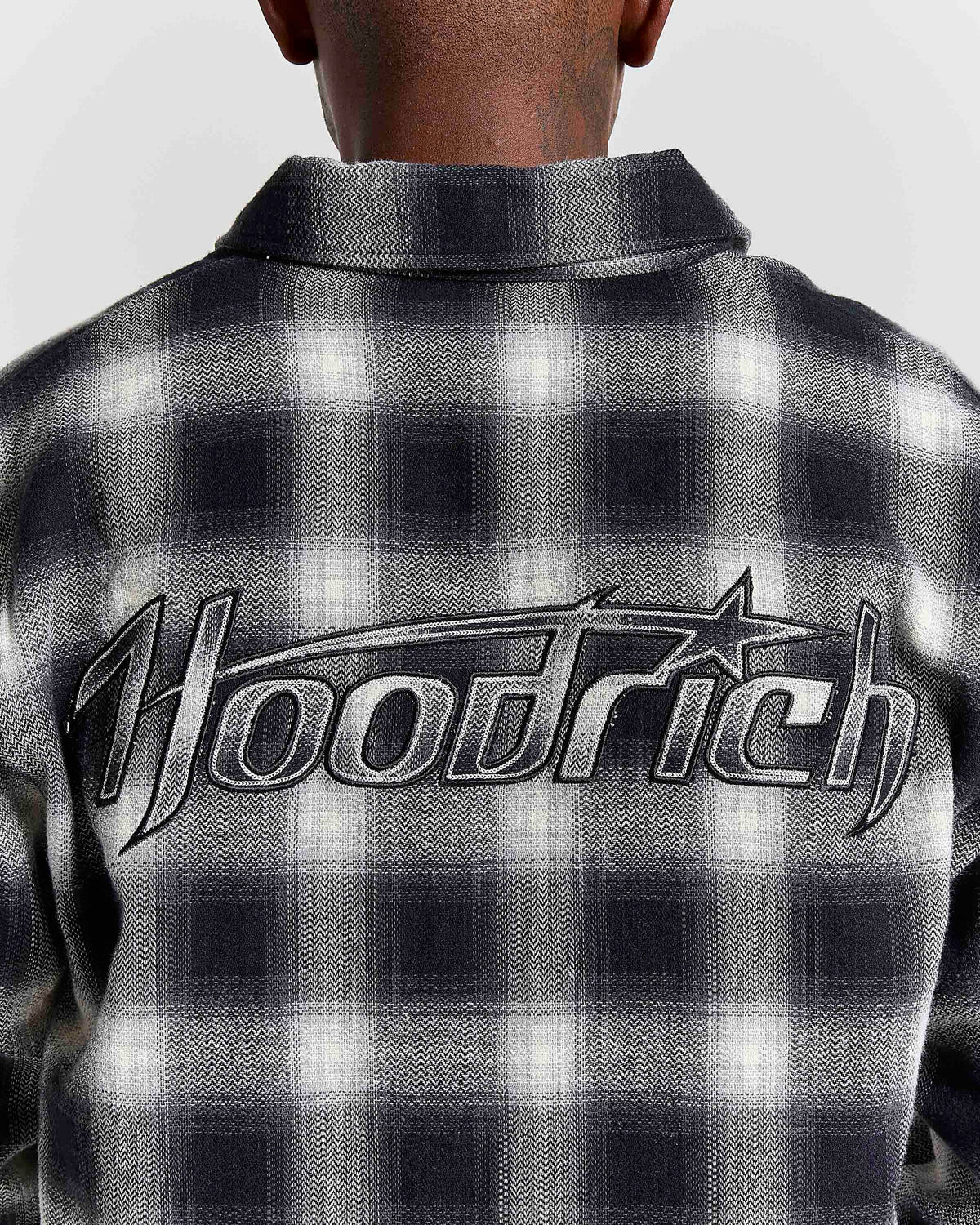 Close-up back view of a person wearing a black and white plaid hooded shirt with a large 'Hoodrich' logo across the back.