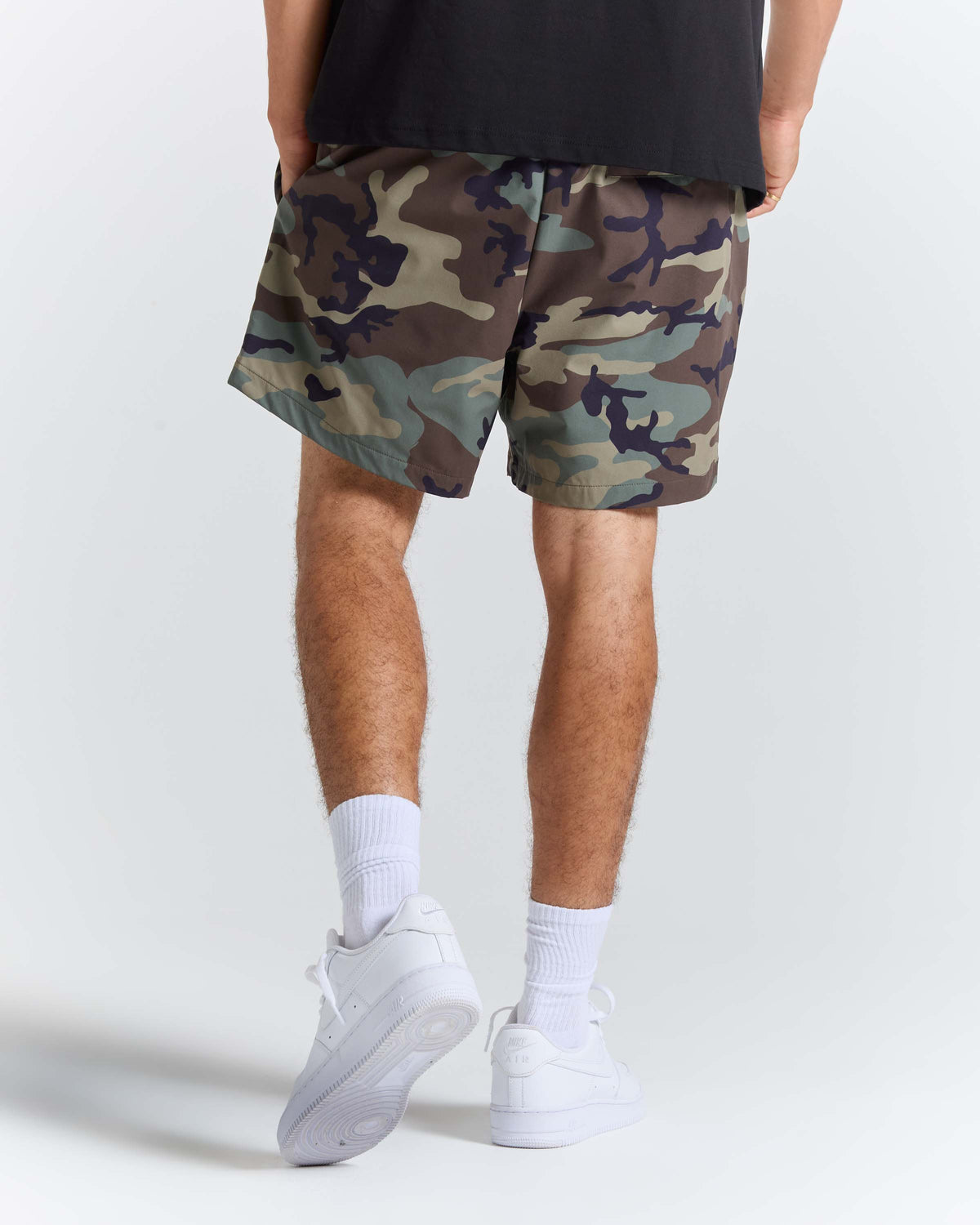A person shown from the waist down wearing camouflage shorts, white crew socks, and white sneakers against a light gray studio background.