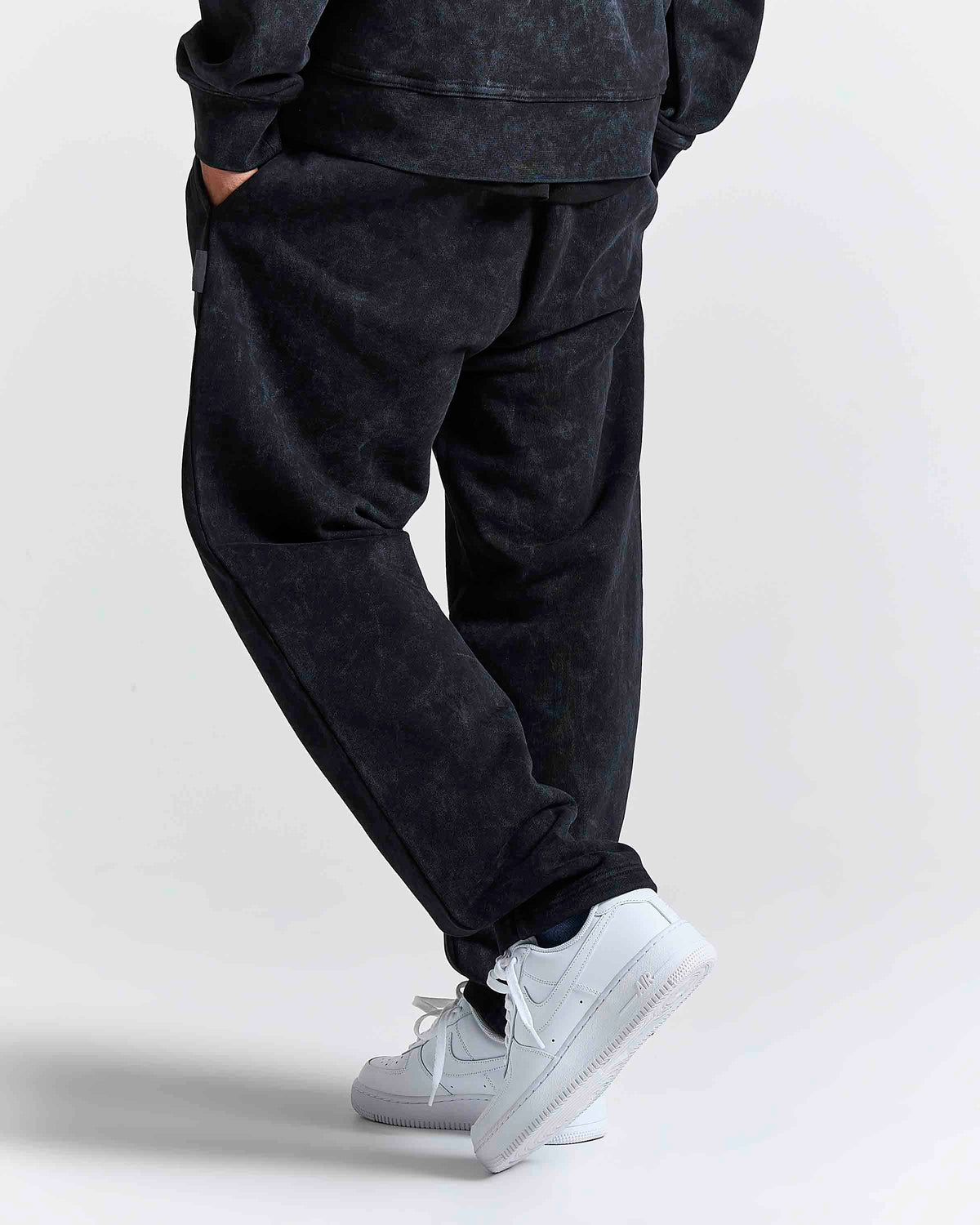 A person wearing dark washed jogger sweatpants and white sneakers, shown from the waist down in a studio setting.