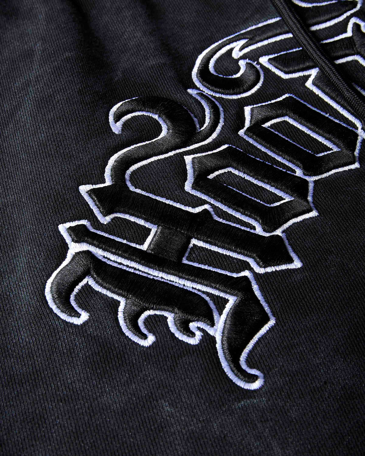 Close-up of a black hoodie featuring a large, stylized gothic-style embroidered logo in black and white.