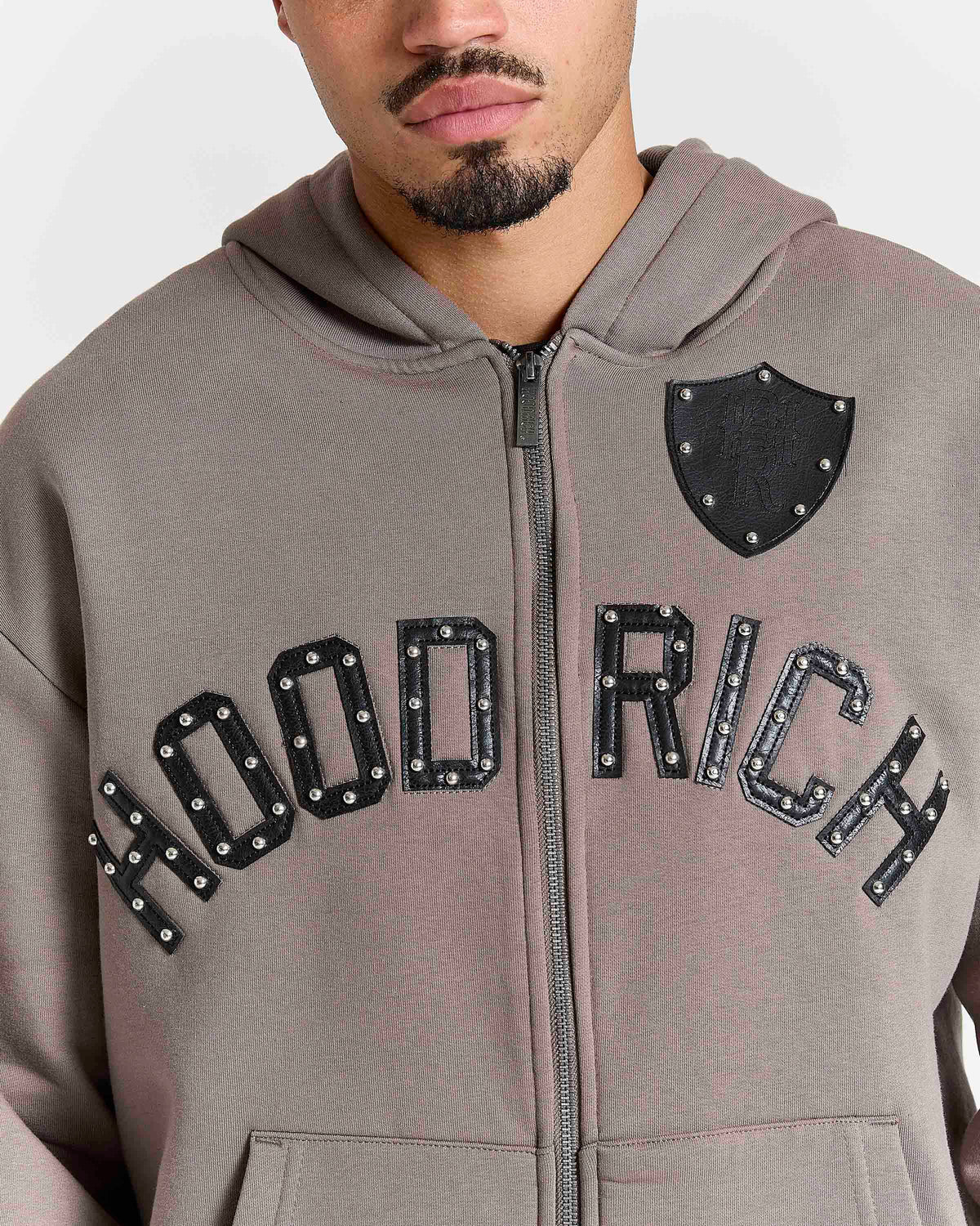 Displays a model wearing the Brown 'Hoodrich' branded men's Varso Studs Full Tracksuit featuring the details on the hoodrich branding 
