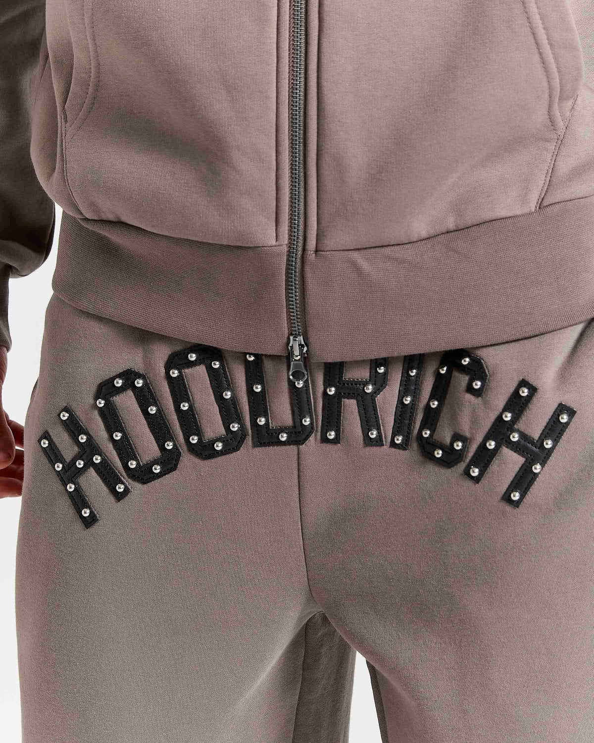 Displays a model wearing the Falcon Black 'Hoodrich' branded Varso Studs Oversized Wide Leg Jogger featuring the details on the branding 