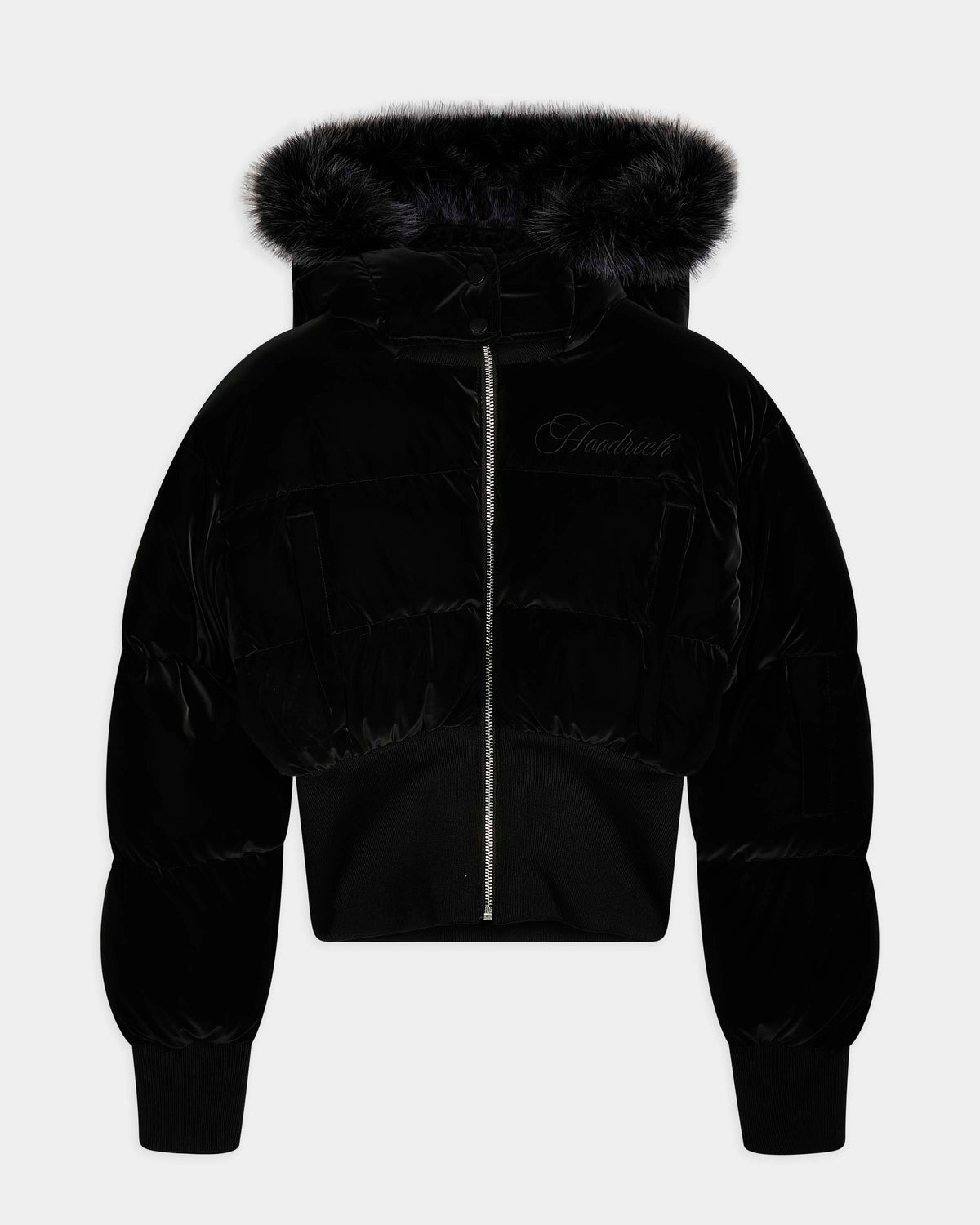 A black cropped puffer jacket with a plush faux-fur trimmed hood, featuring a front zipper, ribbed cuffs, and a subtle embroidered logo on the left chest, shown against a light gray background.