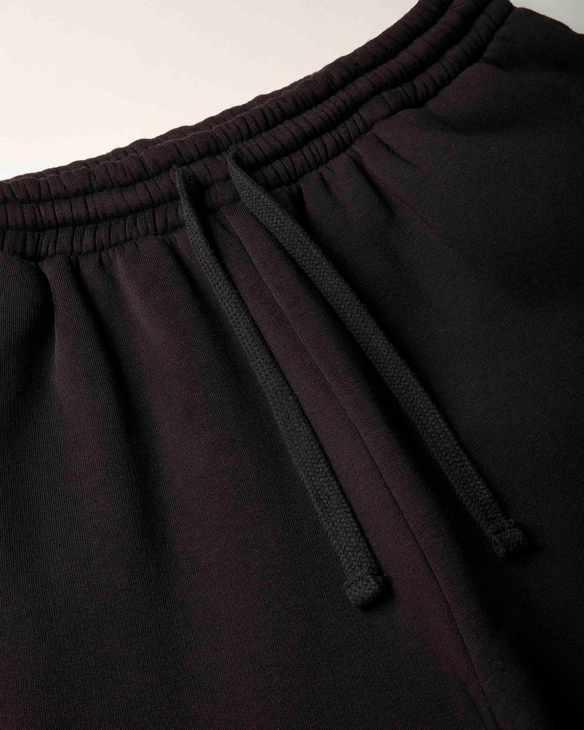 Close-up of black sweatpants showing the elastic waistband, drawstring, and fabric texture.