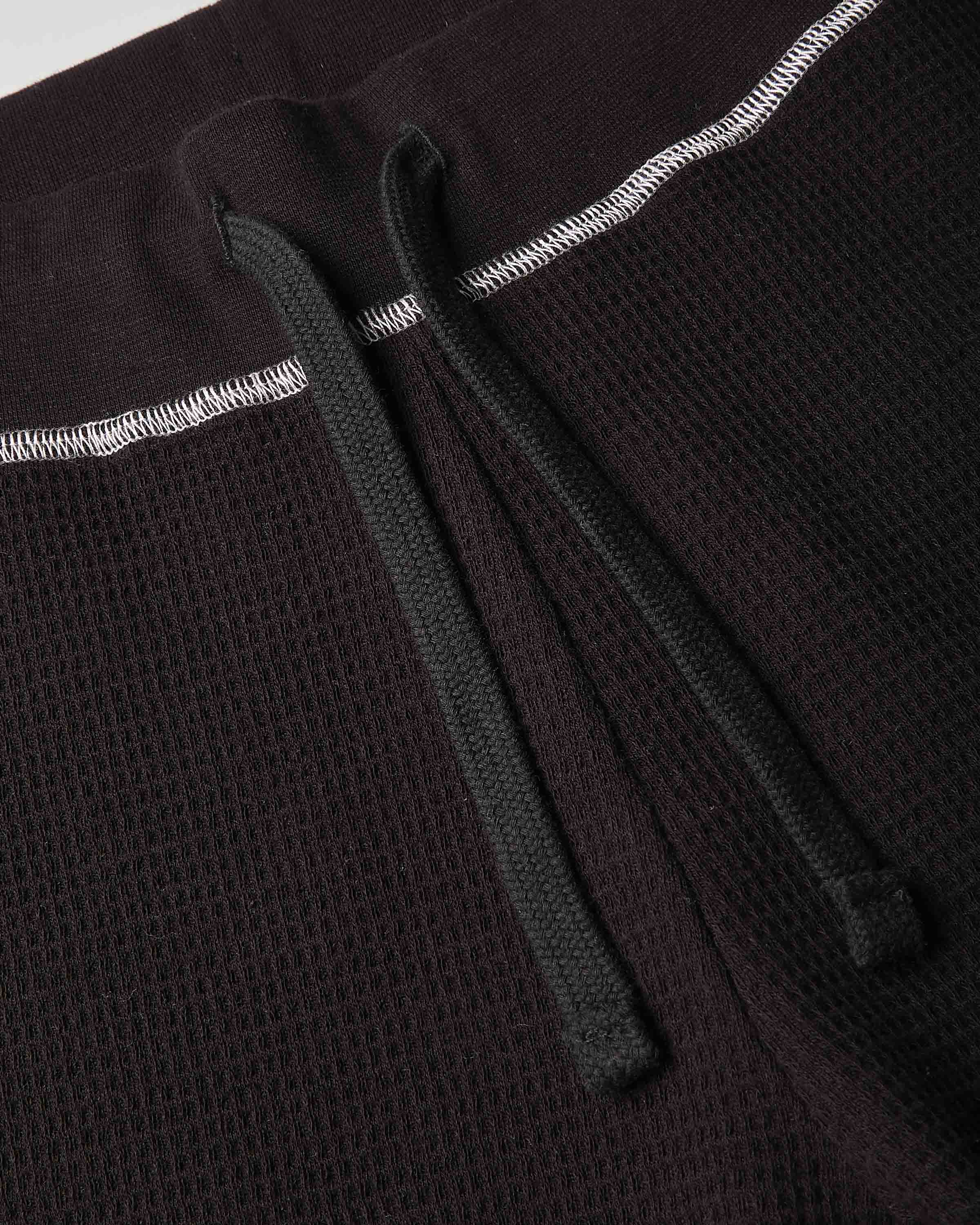 Close-up detail of a dark brown waffle-knit garment, showing a black drawstring and white contrast stitching.