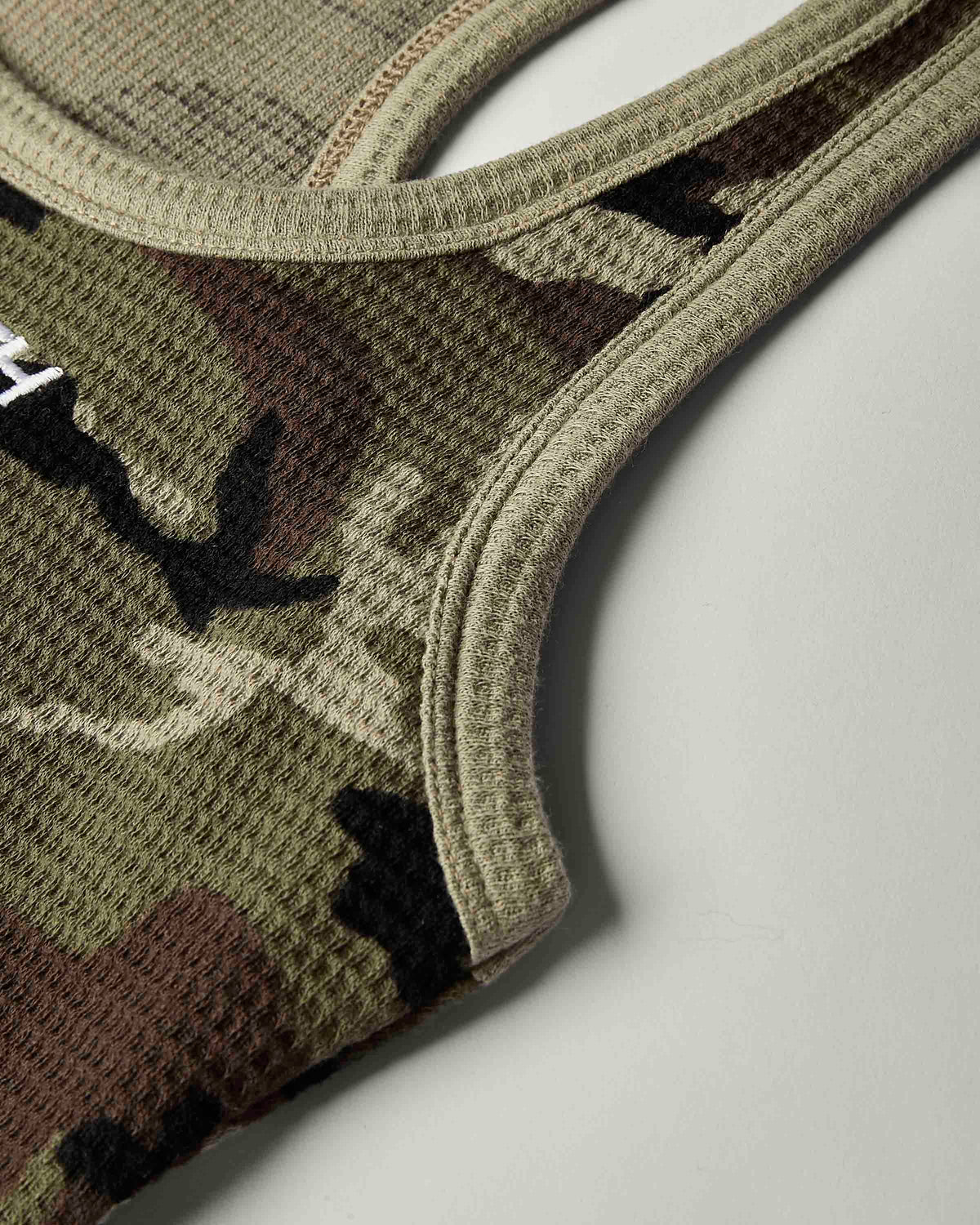Close-up of a waffle-knit athletic top in a camouflage pattern, showing the textured fabric and ribbed trim on a light gray background.