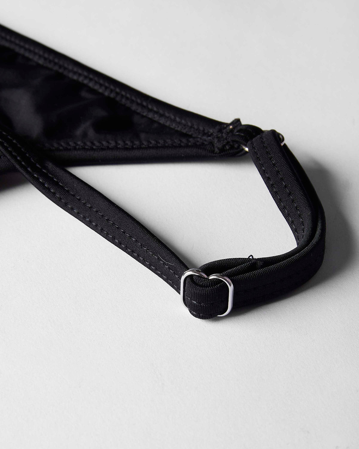 Close-up of a black adjustable strap with a silver metal buckle on a light gray background.