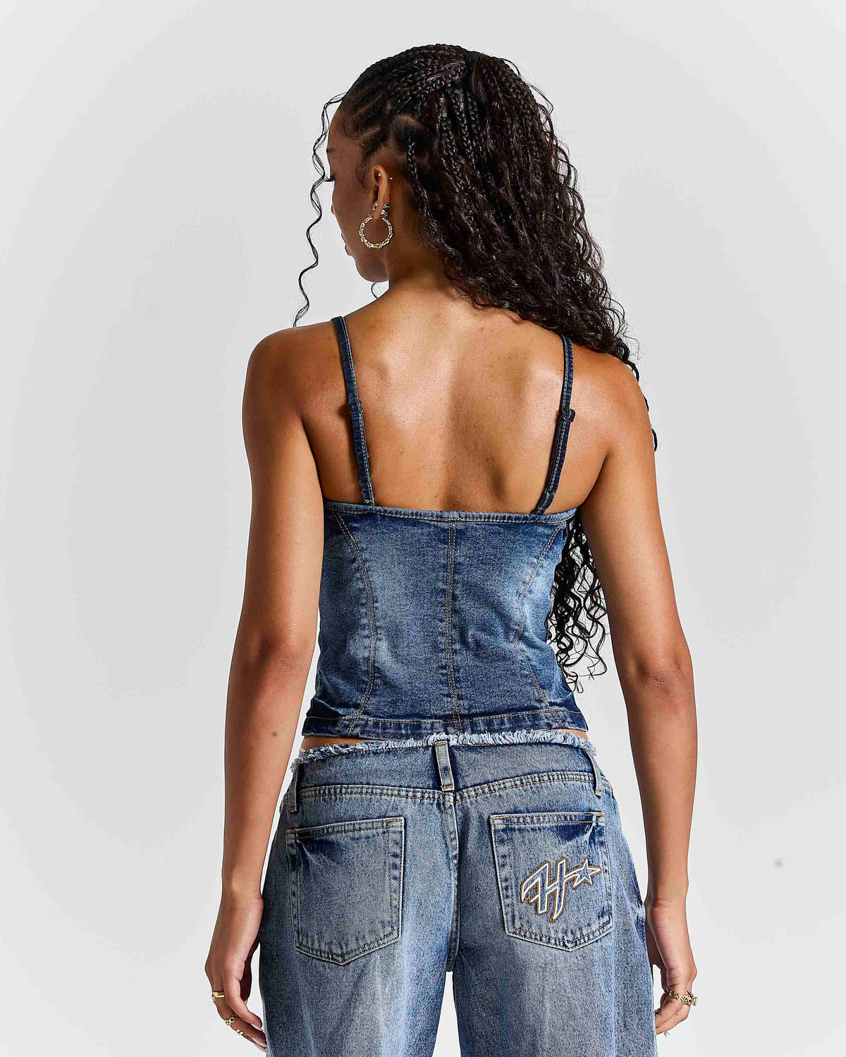 A woman shown from the back wearing a blue denim camisole top and matching denim pants against a light gray studio background.