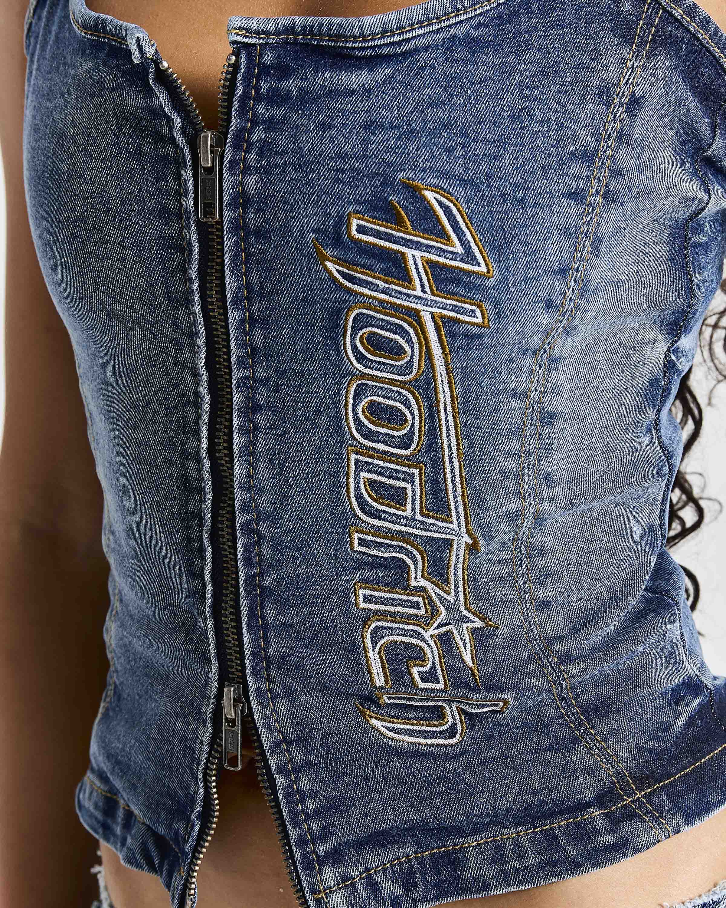 Close-up of a blue denim zip-front top with large metallic embroidered 'Hooded' lettering on the front, worn by a model.