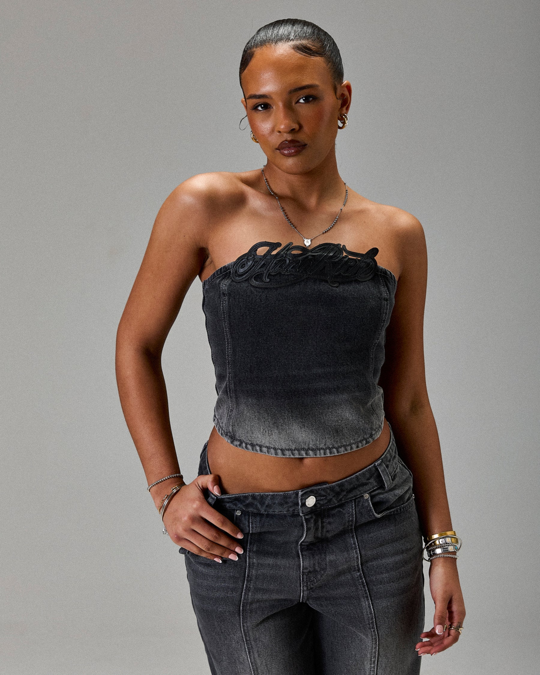 Woman wearing a black strapless top and high-waisted jeans against a gray background