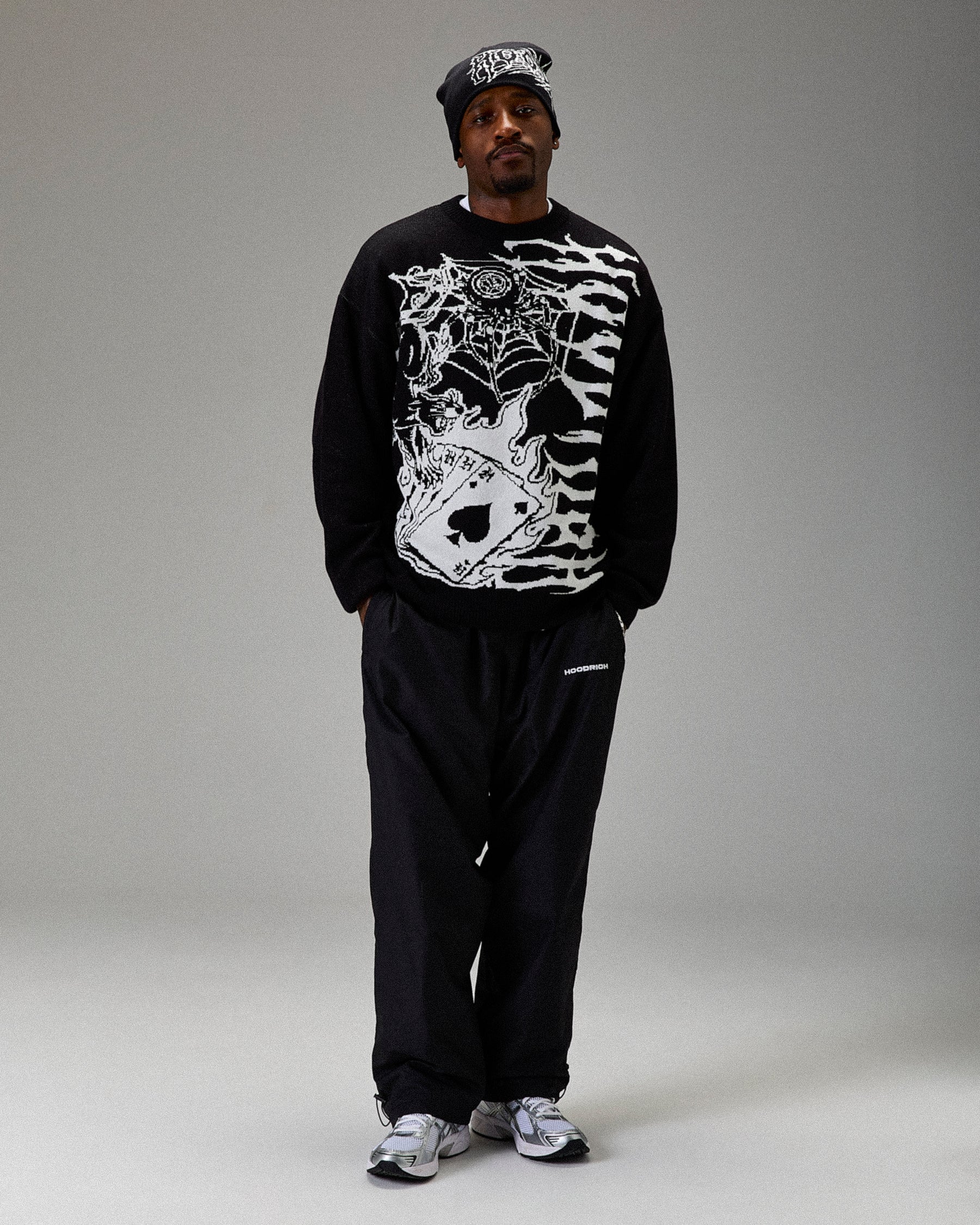 Person wearing a black sweatshirt with white graphic design and black pants on a gray background