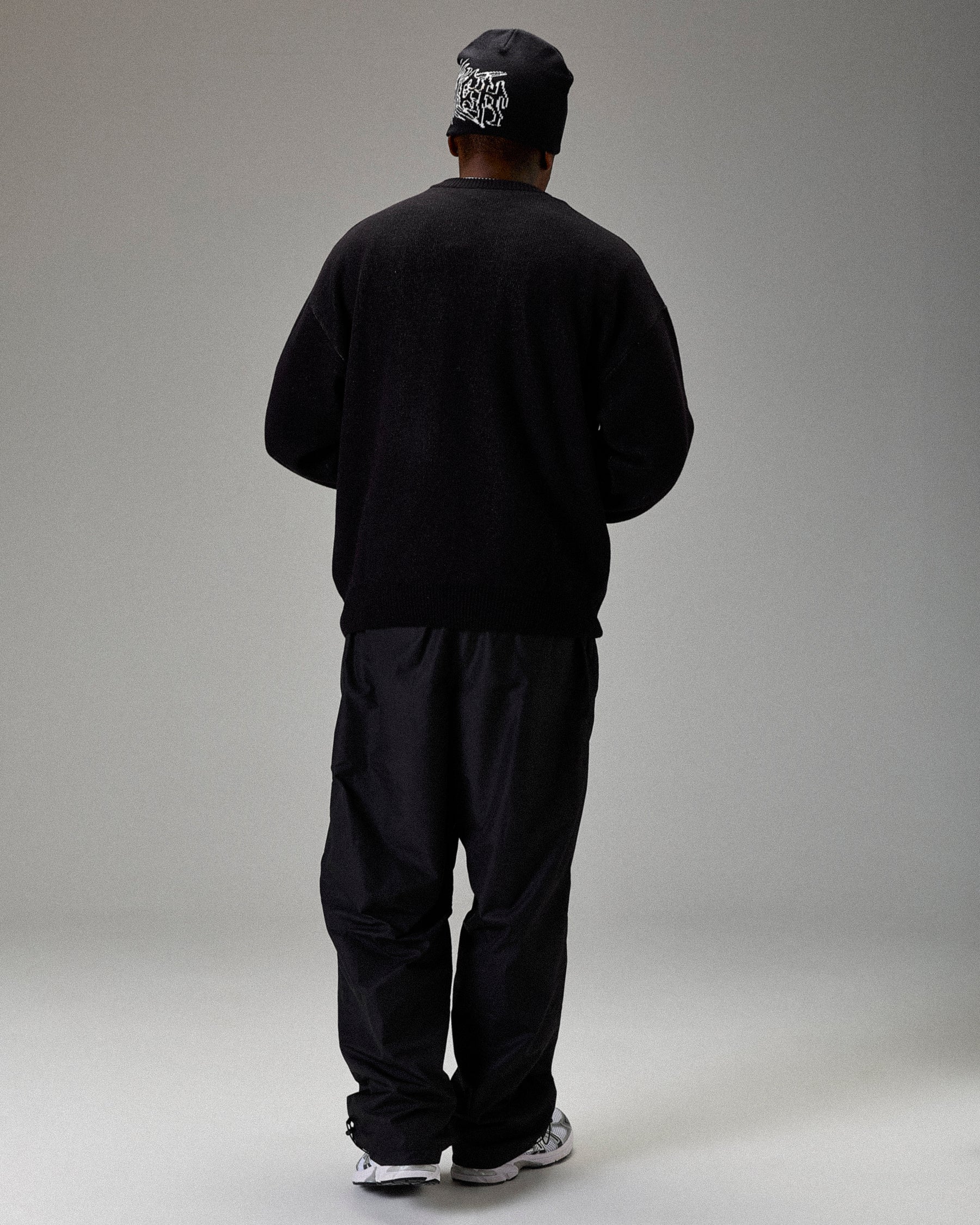 Person wearing a black outfit with a cap on a gray background