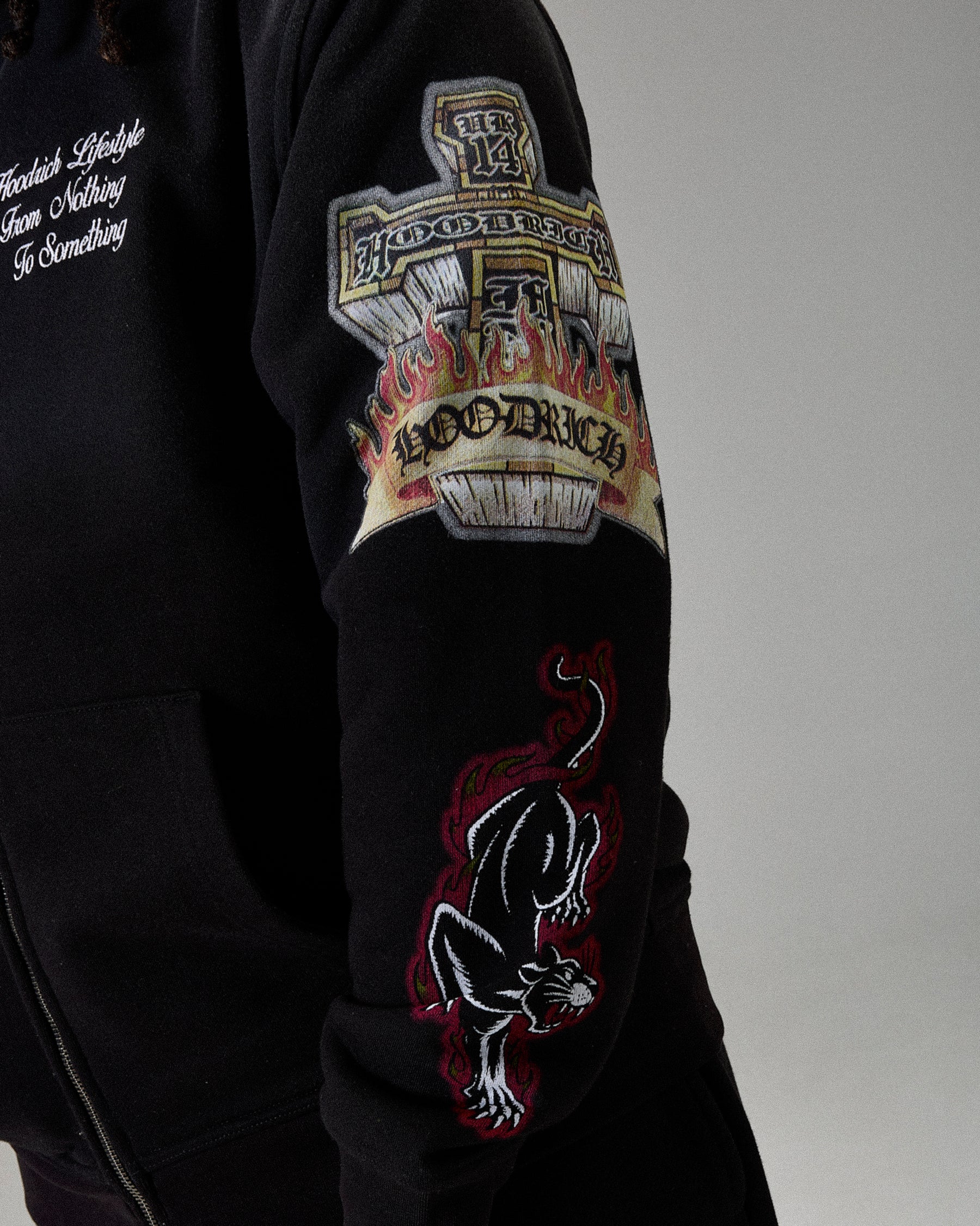 Black hoodie with embroidered designs on the sleeve against a gray background