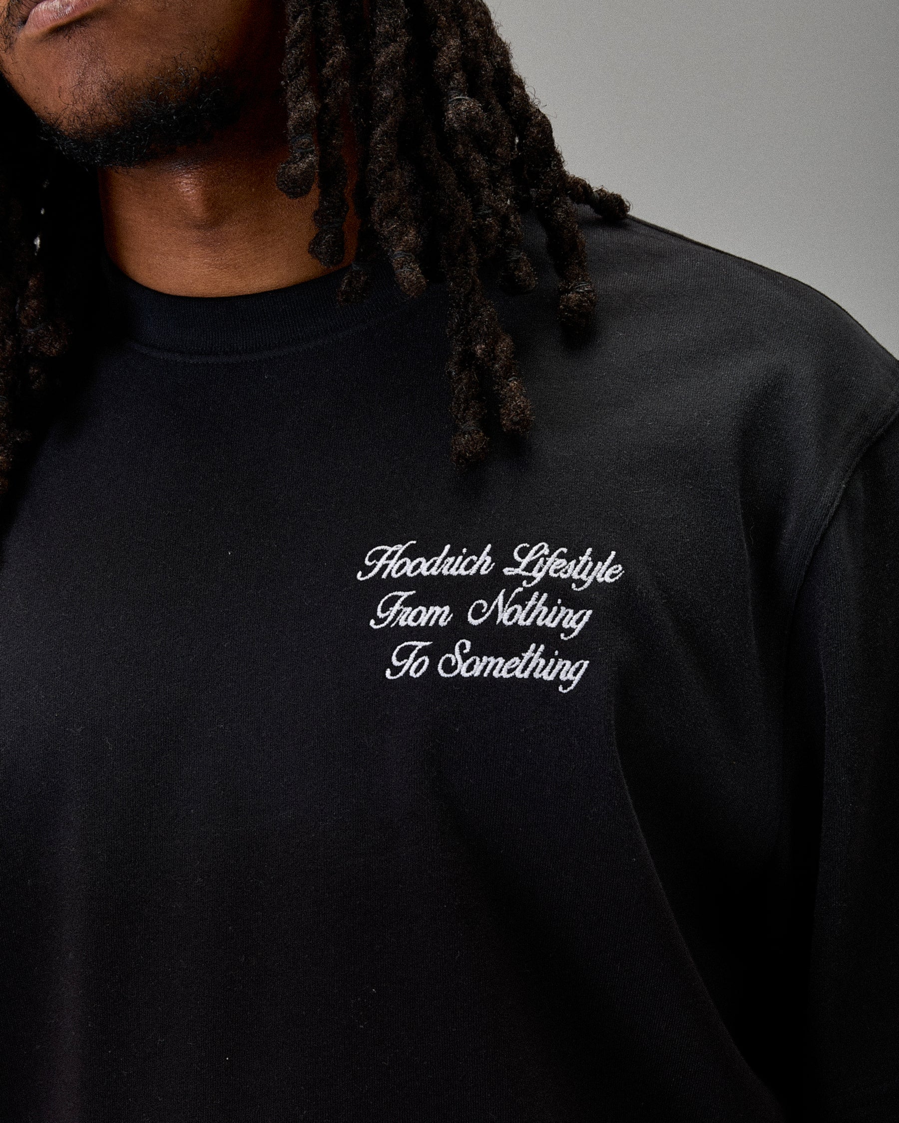 Black t-shirt with white text saying "Hoodrich Lifestyle From Nothing To Something" worn by a person, on a neutral background