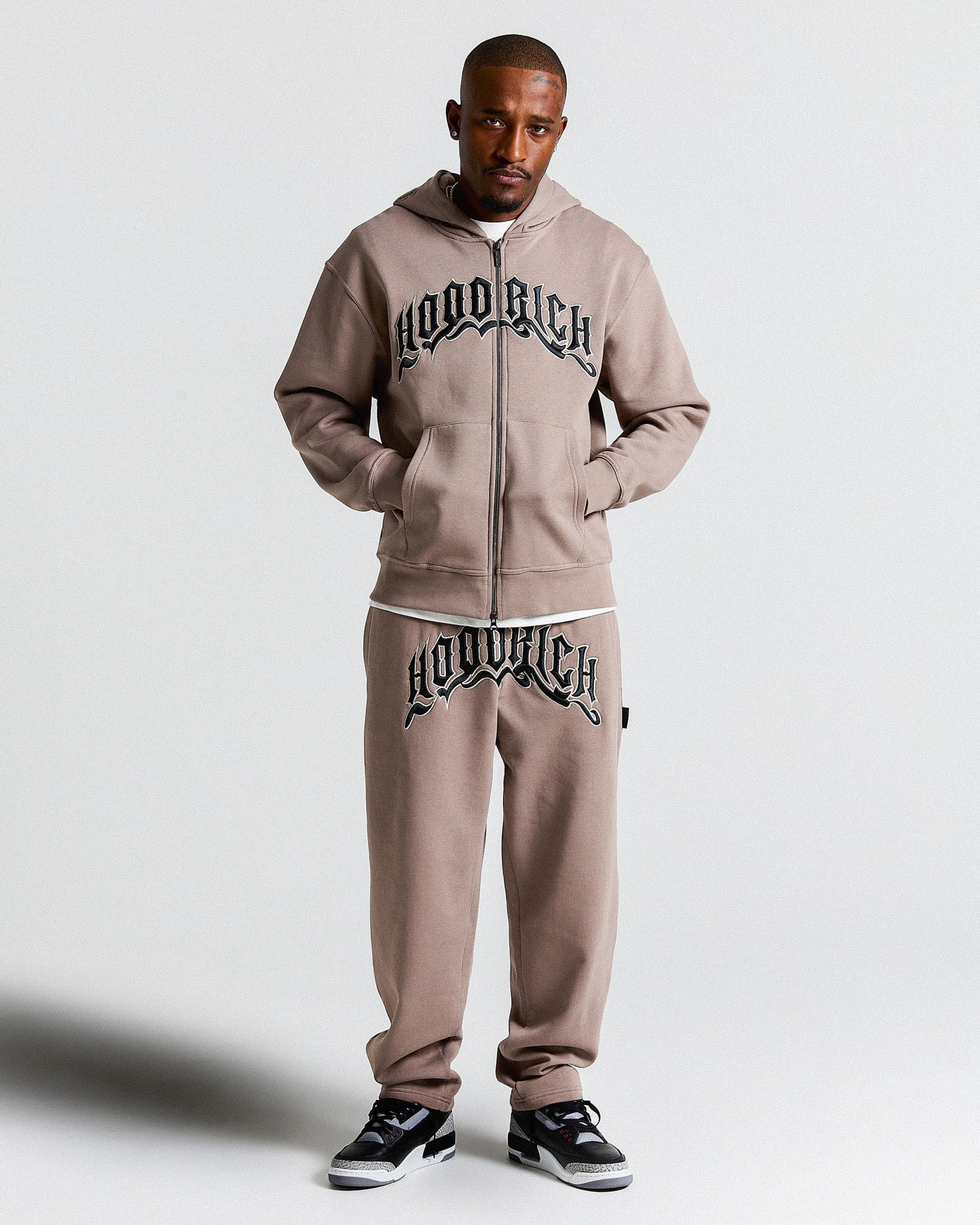 Man wearing a beige tracksuit with 'HOODRICH' branding on a white background