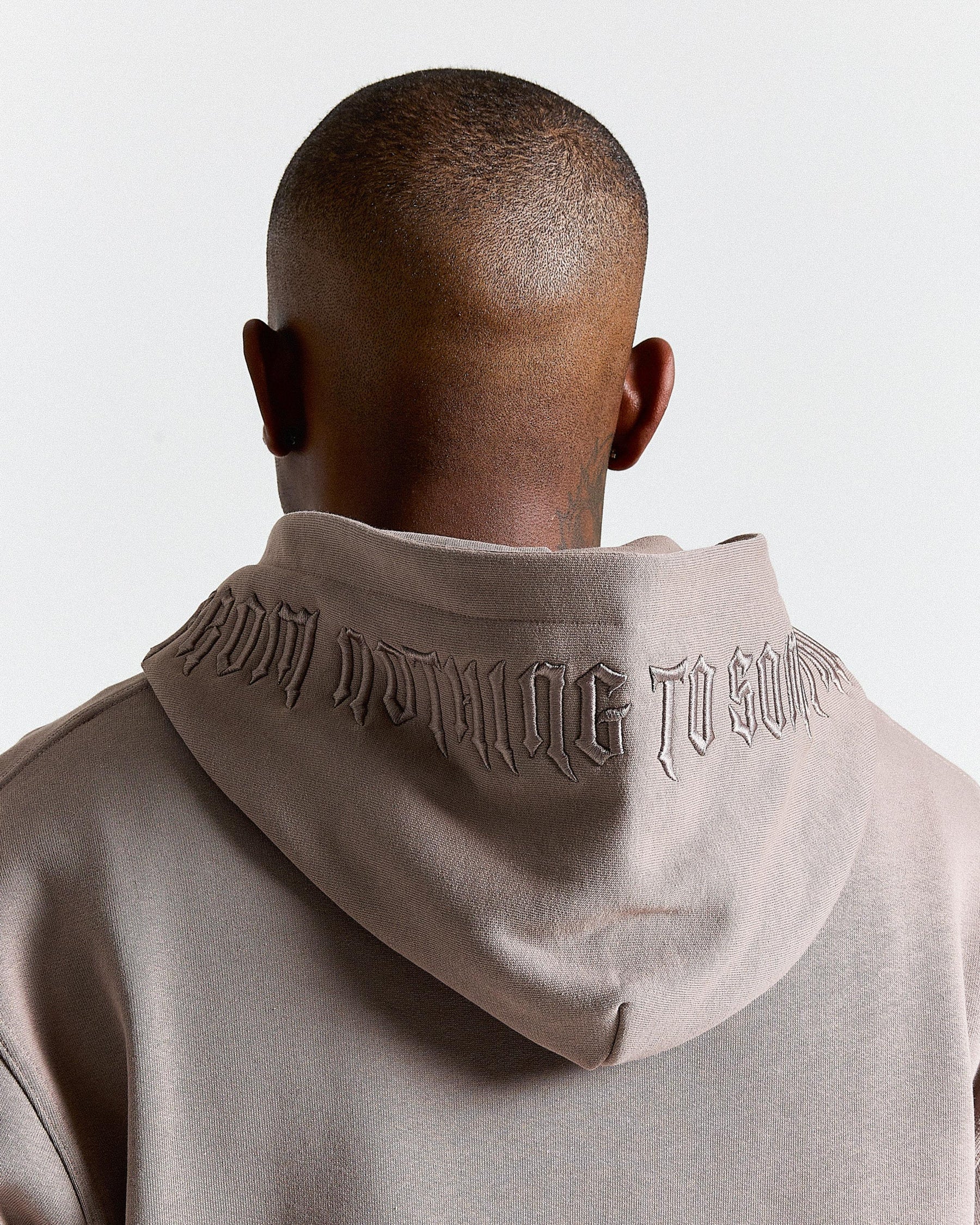 Person wearing a beige hoodie with text on the back against a light gray background