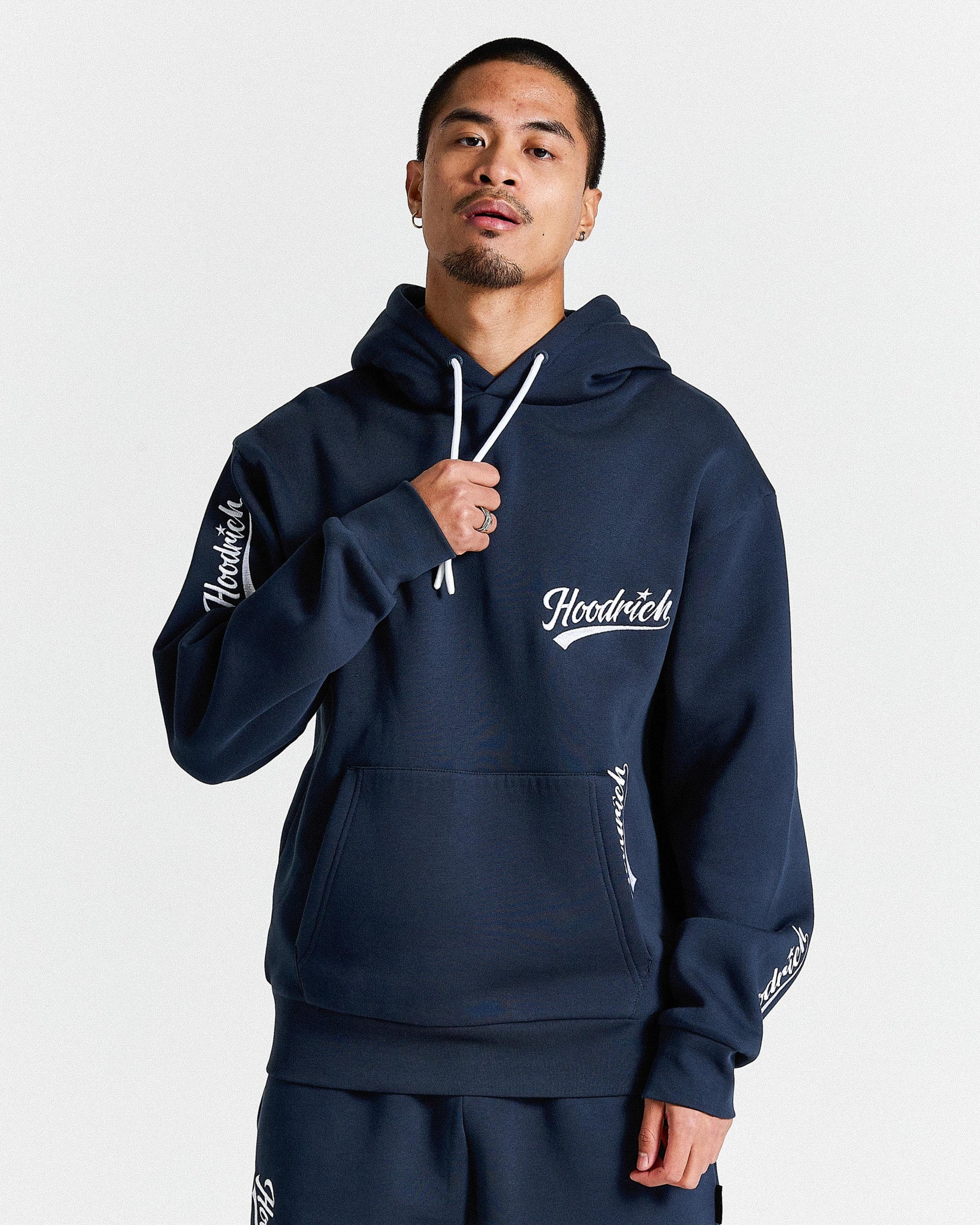 Man wearing a navy blue hoodie with branding on sleeves against a white background
