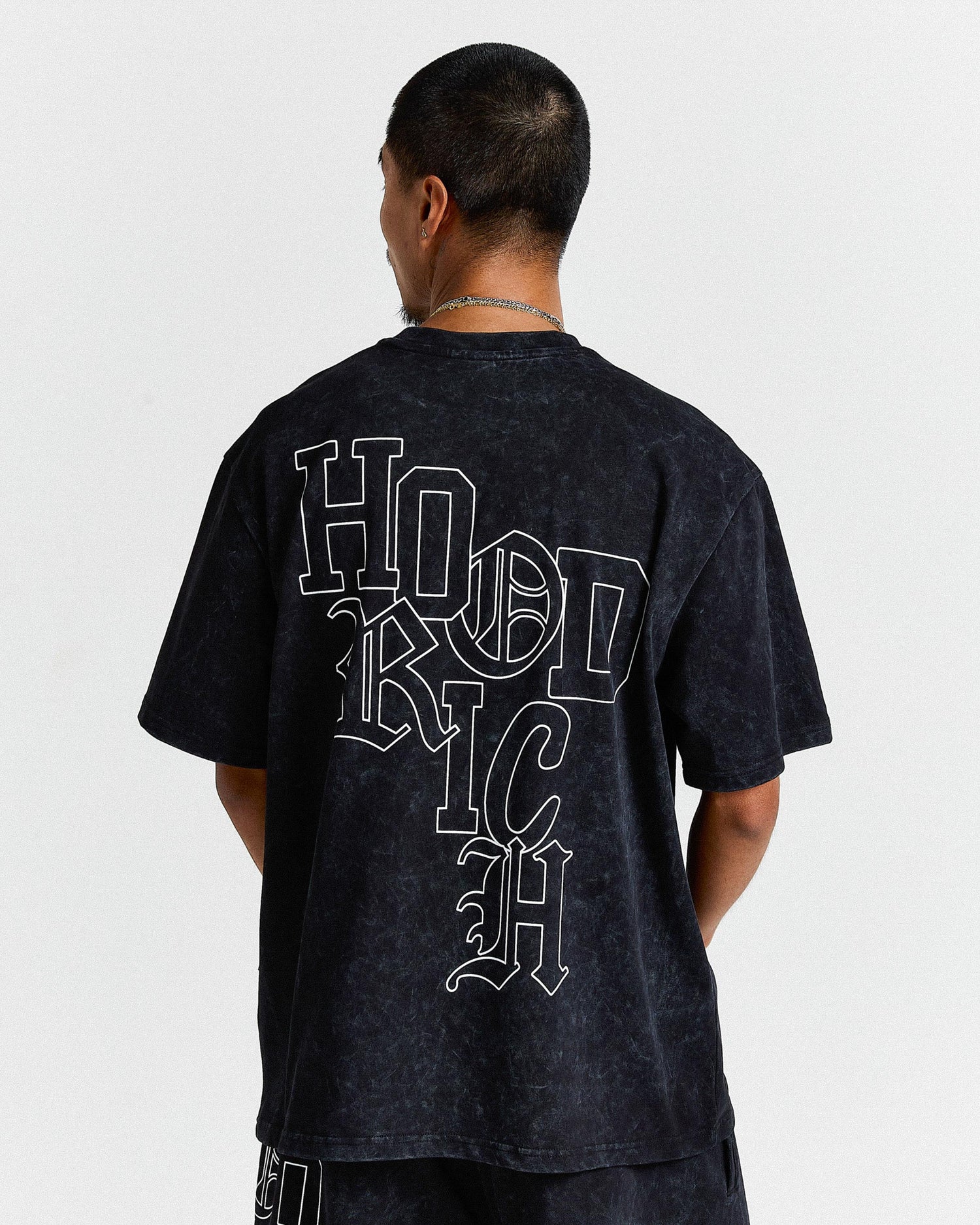 Person wearing a black t-shirt with 'HOOD RICH' text on the back against a white background