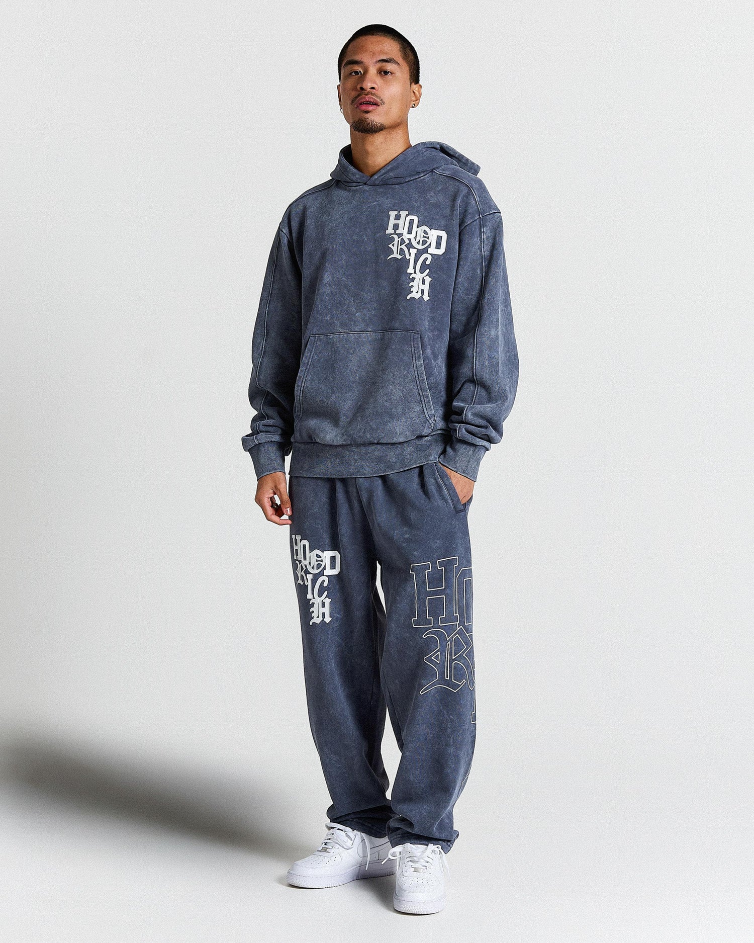 Person wearing a blue hoodie and pants with branding on a white background